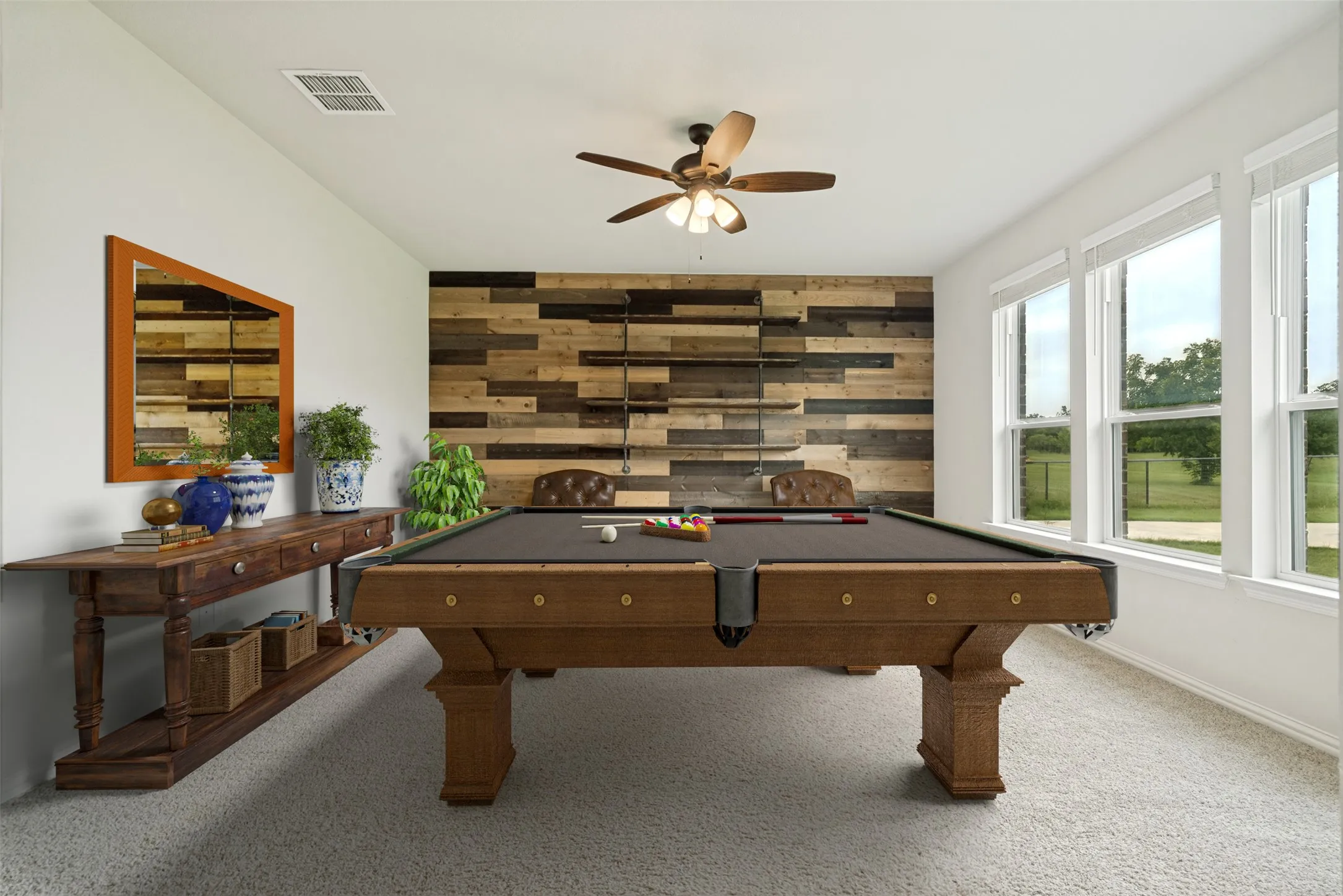 Spacious recreation room featuring a multi-toned wood plank accent wall, large picture windows, light-tone carpeting, a ceiling fan with integrated lighting, and a console table with a framed mirror
