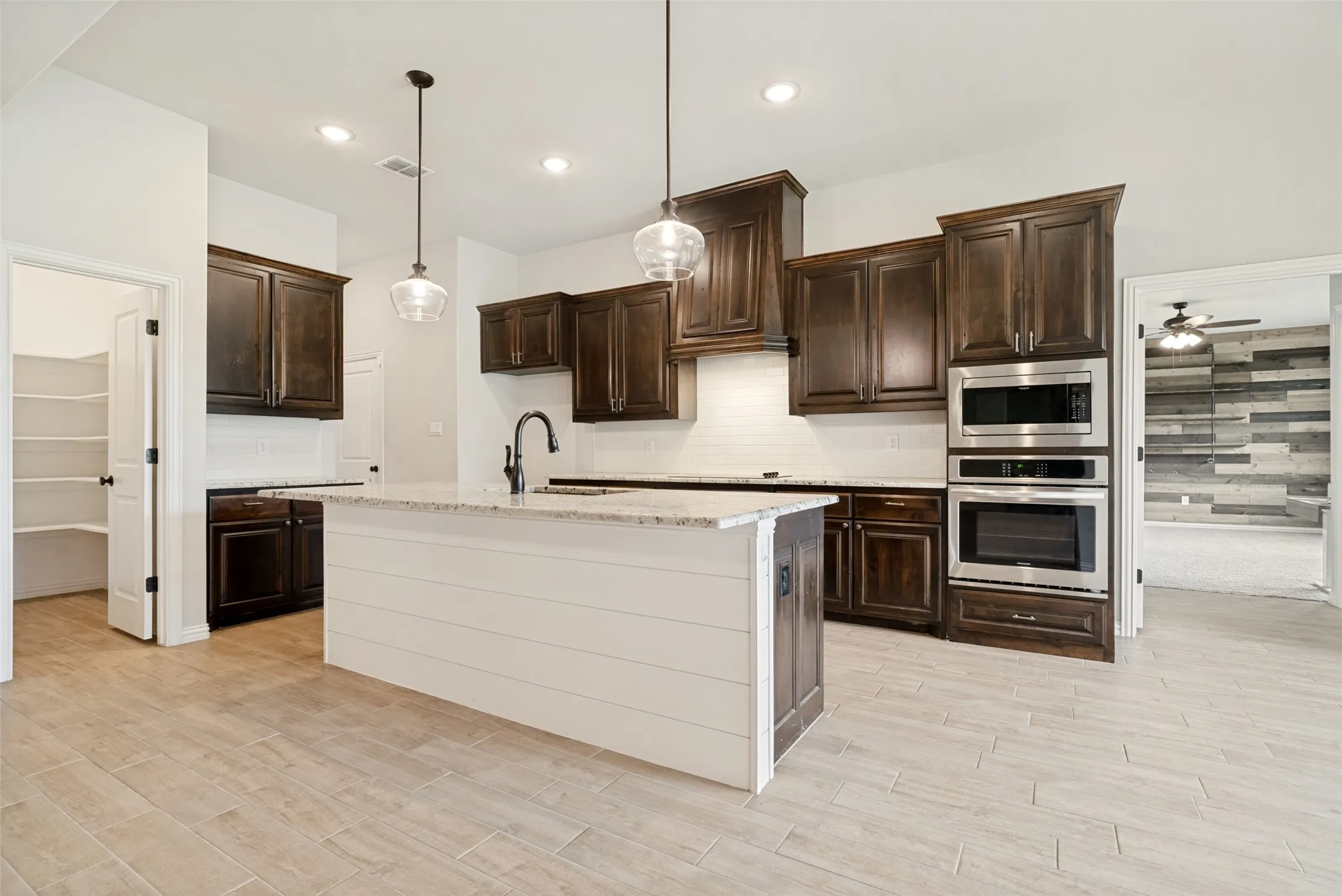 Kitchen featuring dark wood cabinetry, light-colored countertops, stainless steel built-in appliances, and a shiplap island