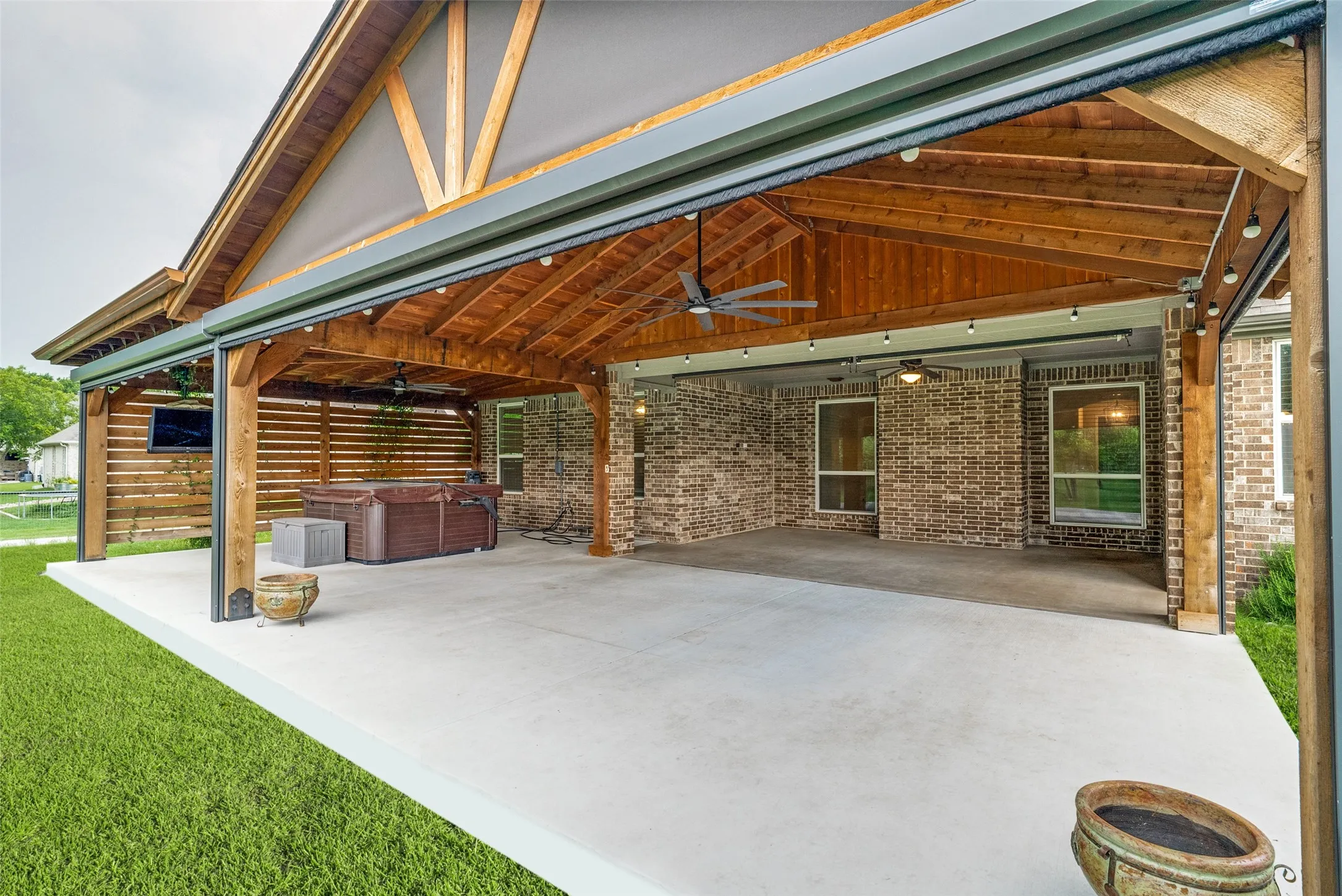 Expansive covered patio featuring a vaulted wood ceiling, ceiling fans, string lighting, and remote screens to completely enclose