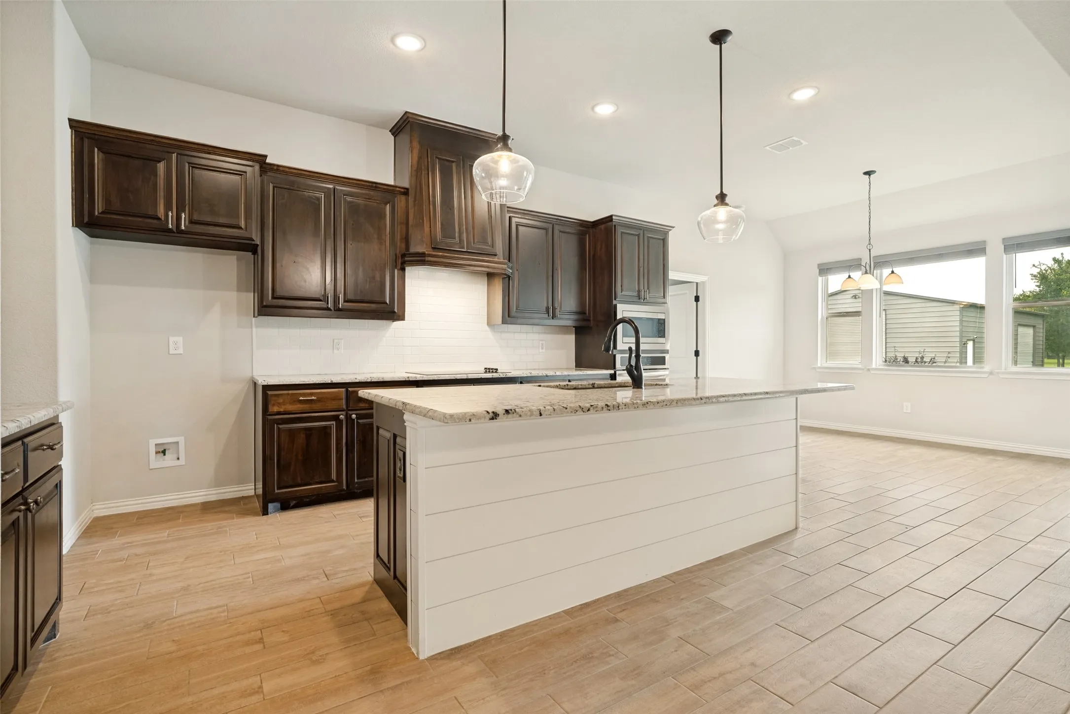 Kitchen featuring wood-finish tile flooring, dark wood cabinetry, white subway tile backsplash, light-colored countertops, and a center island with shiplap-style paneling