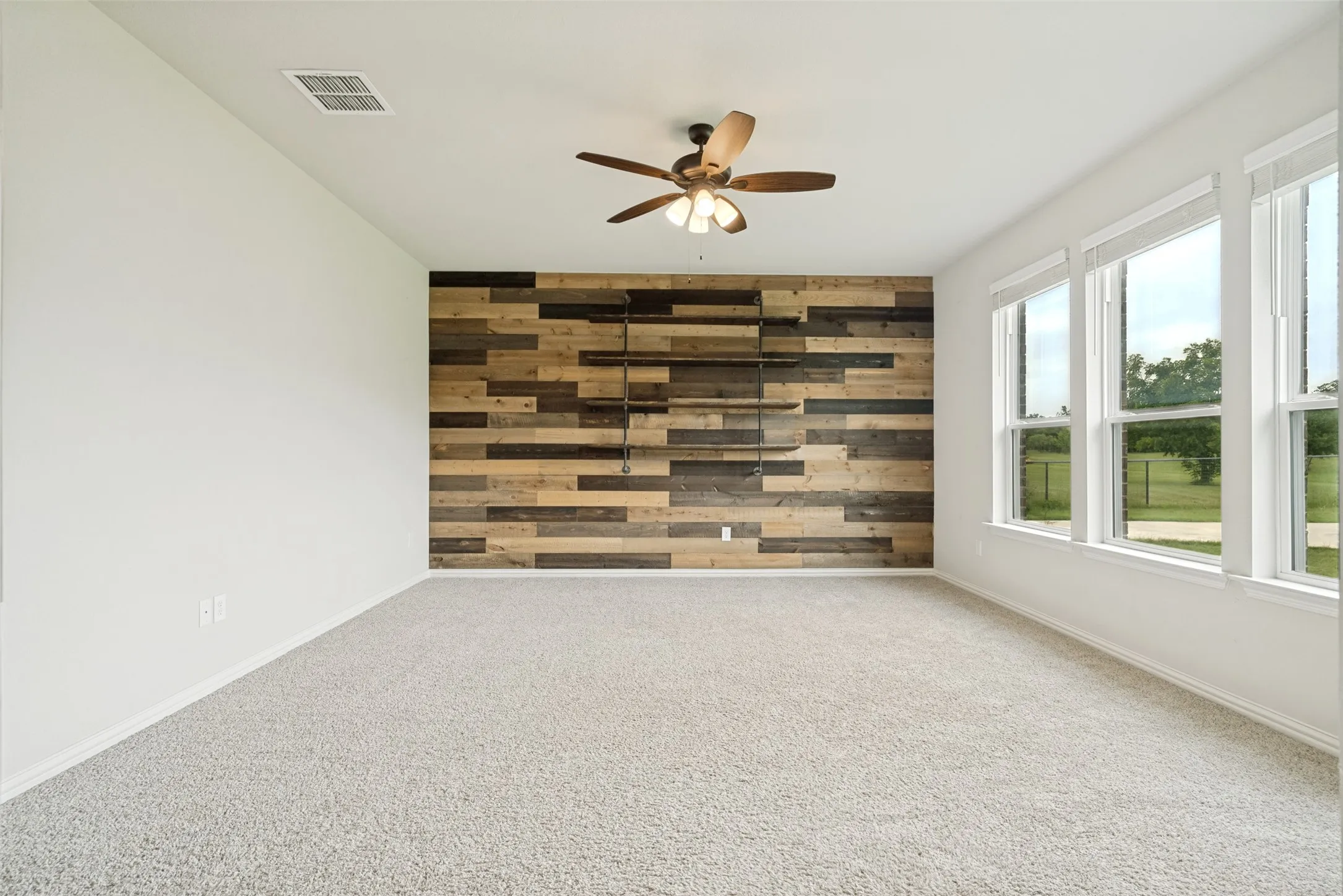 Carpeted room featuring a wood-panel accent wall with built-in shelving, a ceiling fan, and multiple windows
