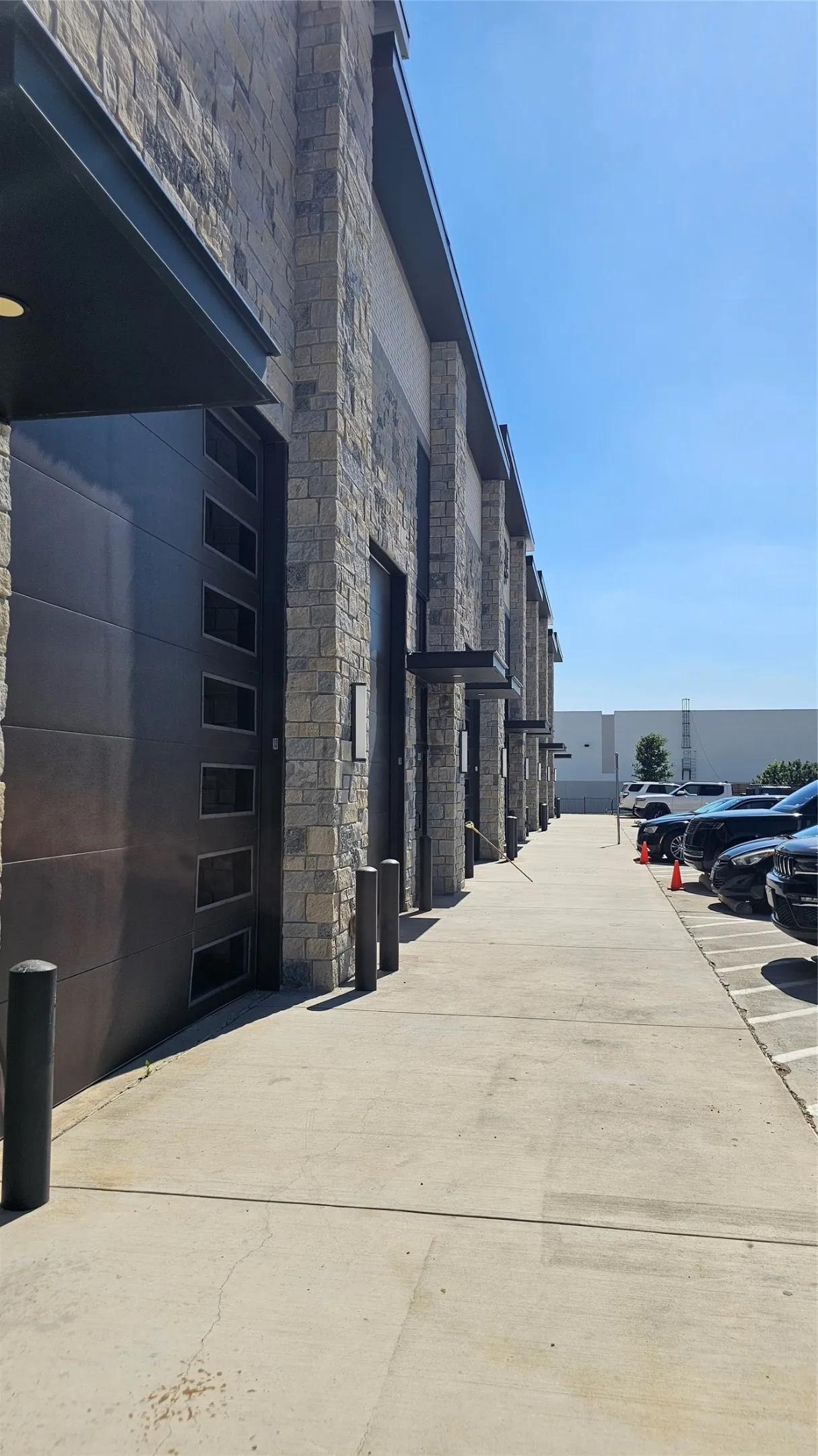 Stone facade building with contemporary dark garage doors, concrete walkway, and parking area