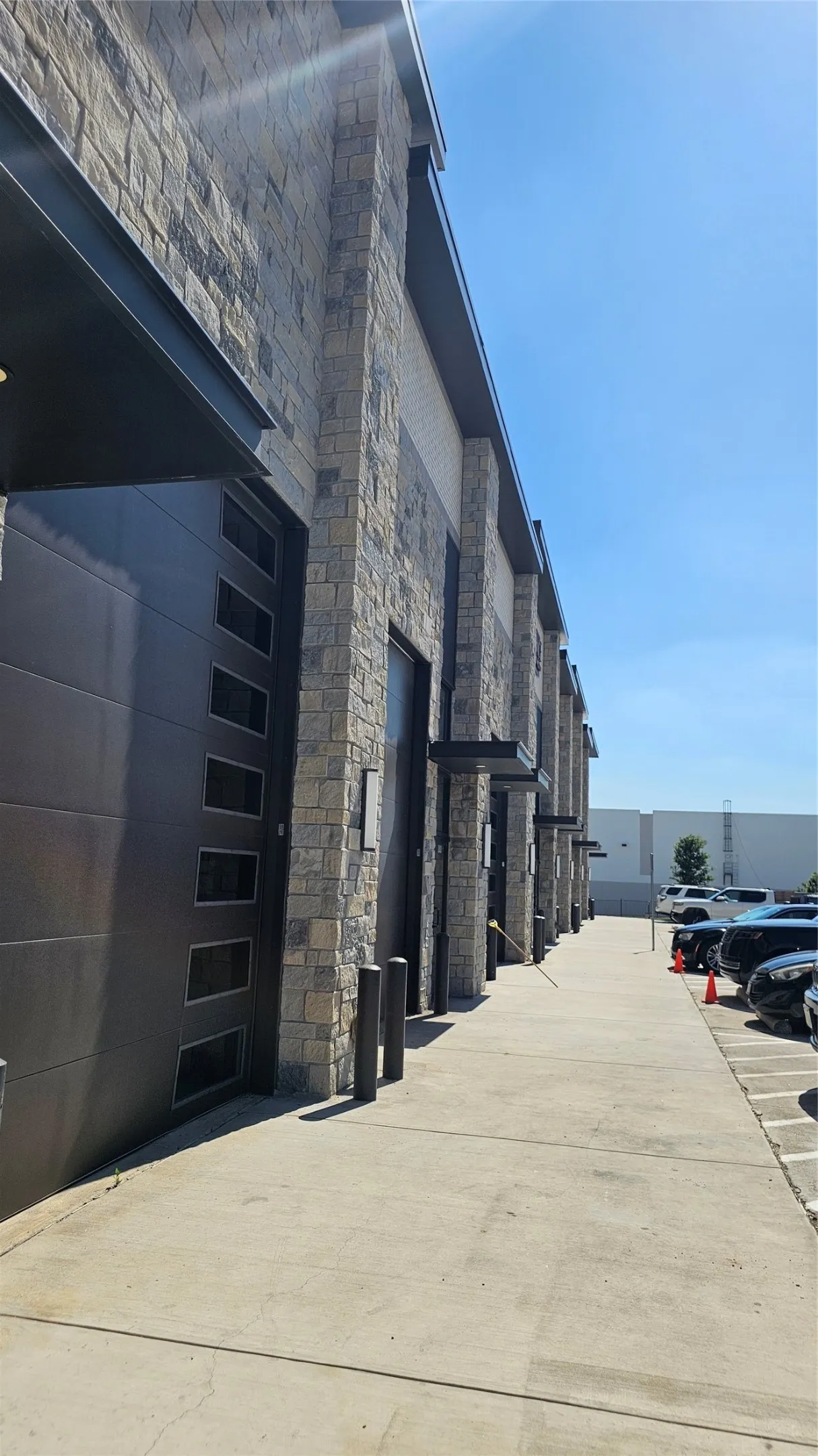 Modern industrial building exterior featuring a stone facade and multiple overhead doors with integrated windows