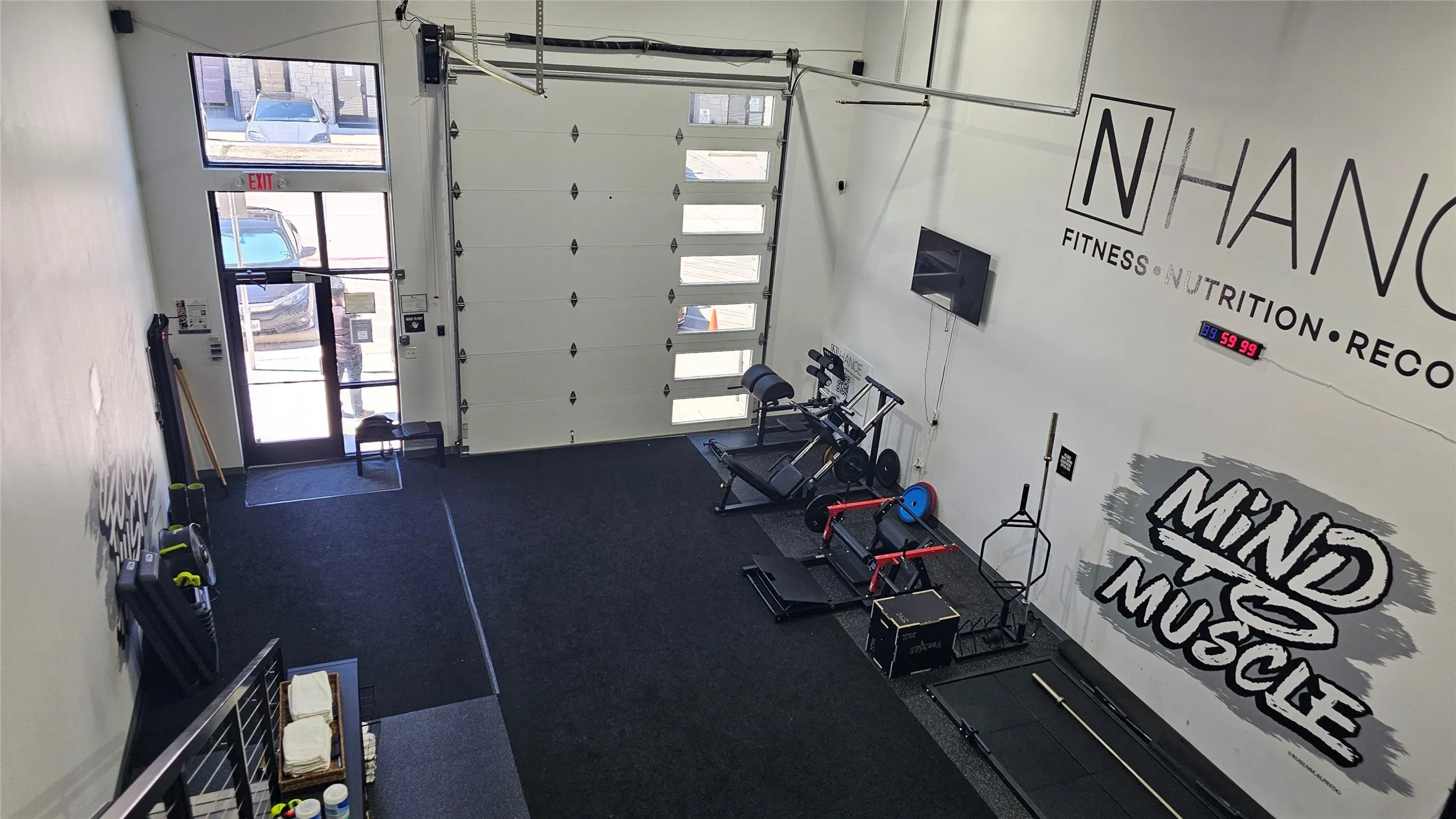 High-ceiling interior space featuring a large glass-paneled garage door, a glass entry door, and dark rubber flooring