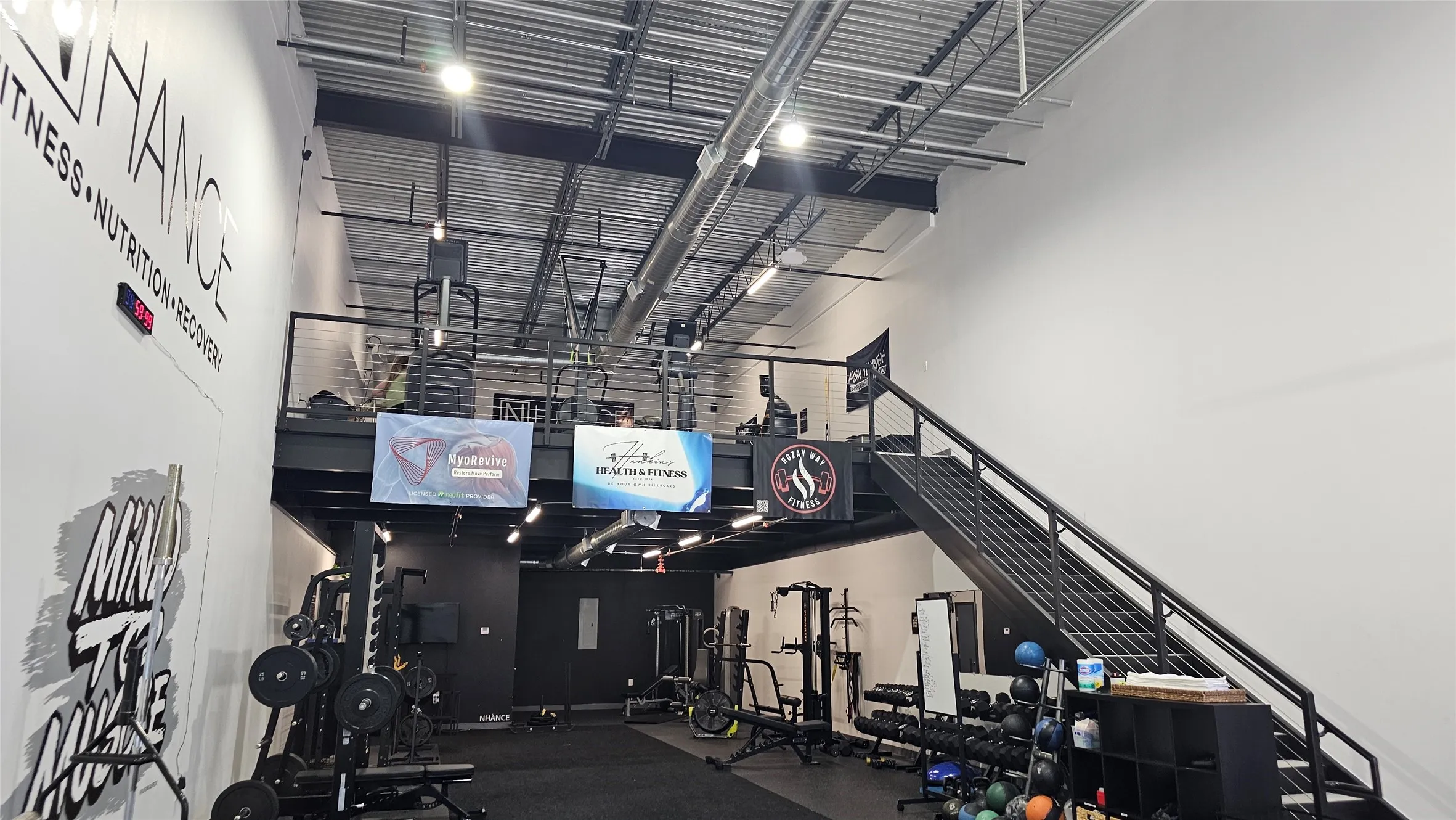Spacious interior featuring a high ceiling with exposed ductwork, a mezzanine level with metal railing, and a black steel staircase