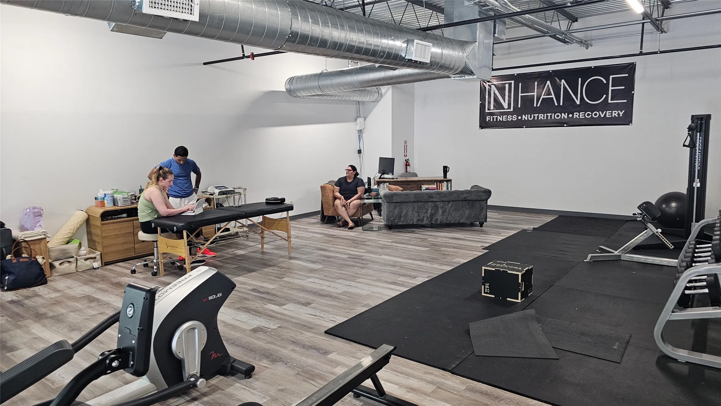 Open-concept commercial space featuring wood-finish flooring, exposed industrial ductwork, and track lighting