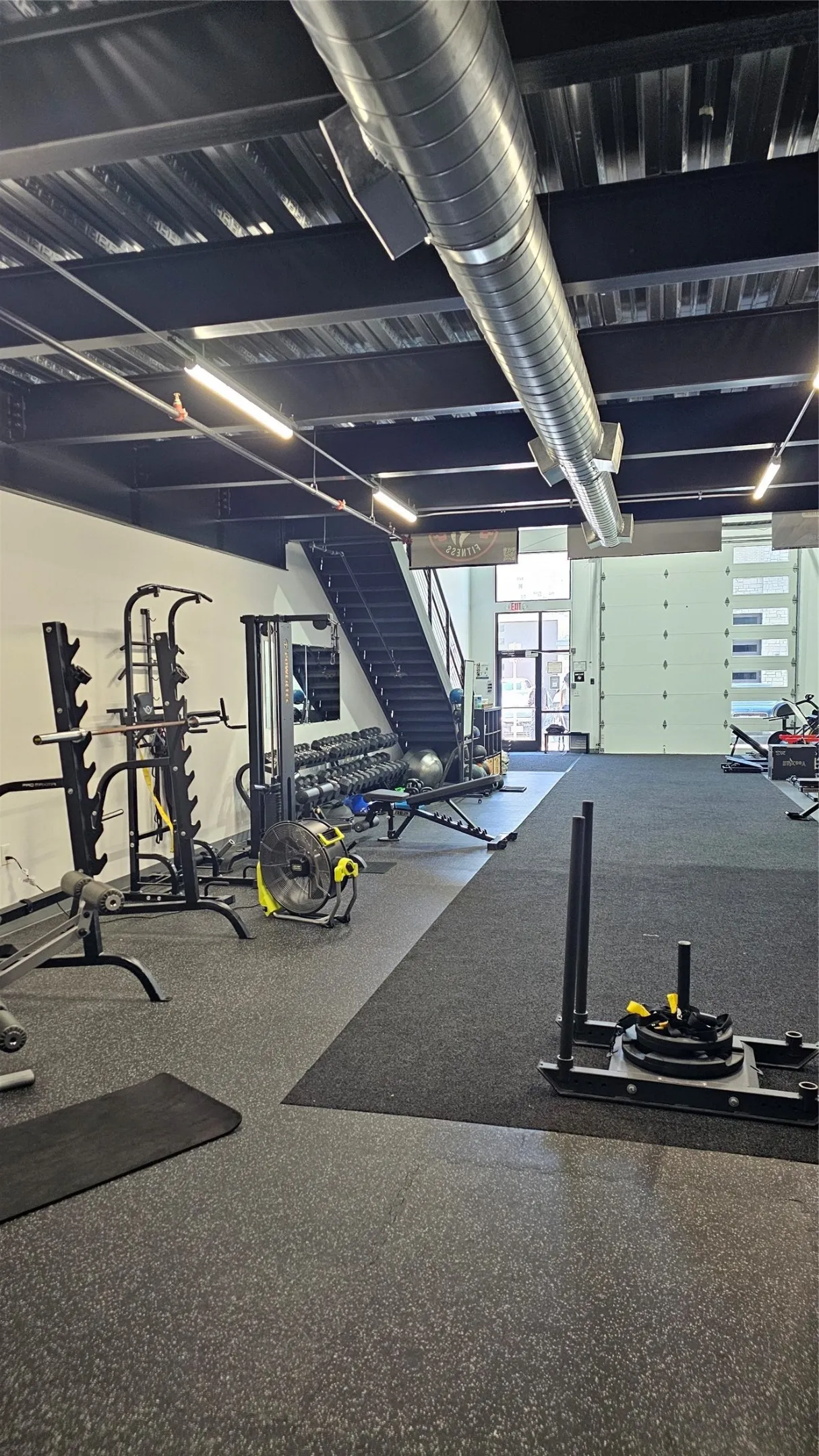 Spacious open-concept interior featuring exposed ductwork, industrial lighting, and a black open-tread staircase