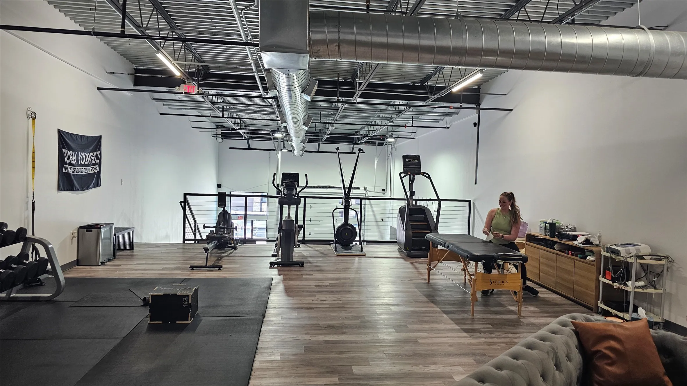 Spacious interior featuring high ceilings with exposed ductwork, recessed lighting, wood-finish flooring, and a dedicated rubber mat exercise area