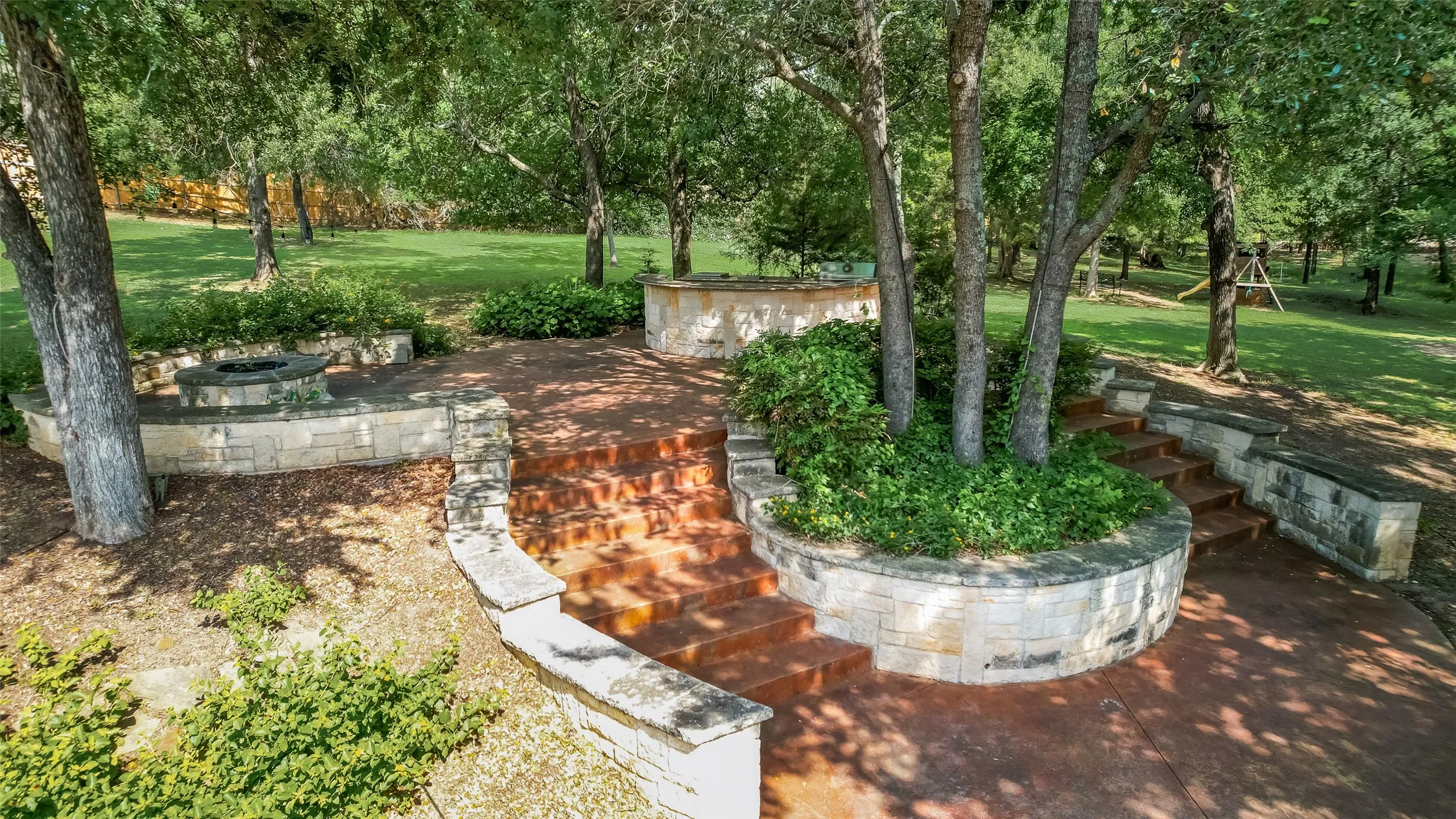 Terraced outdoor area featuring natural stone retaining walls, a built-in fire pit, and mature trees