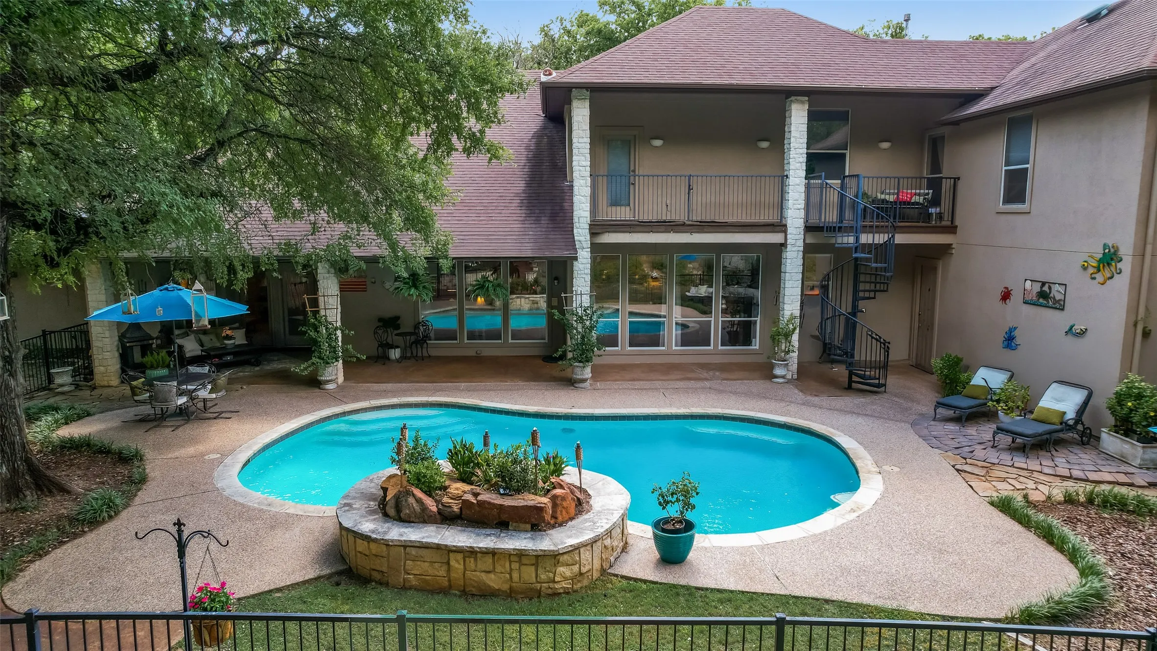 Backyard oasis featuring a curvilinear swimming pool with an integrated planter, exposed aggregate decking, and mature landscaping