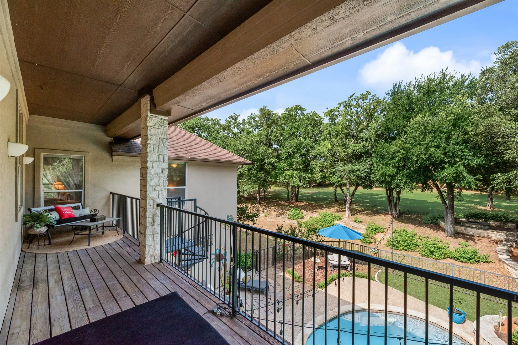 Covered outdoor balcony featuring wood-finish decking, black metal railings, and a stone-clad pillar