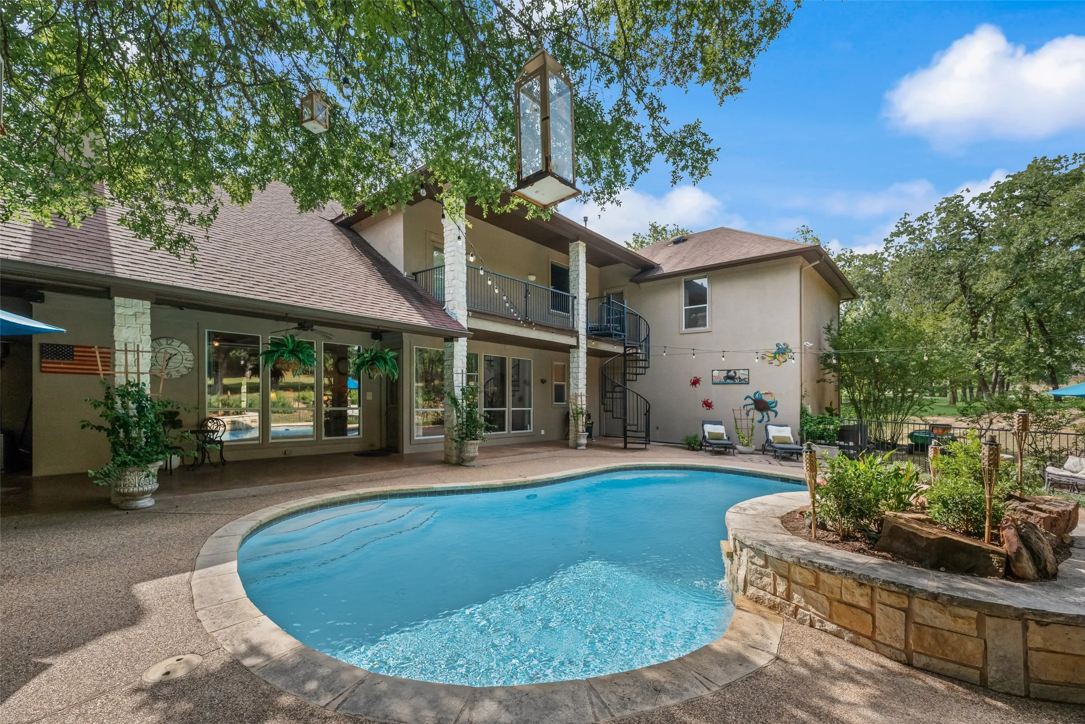 Expansive backyard featuring a freeform swimming pool, flagstone-capped planter with integrated landscaping, and a broad aggregate patio