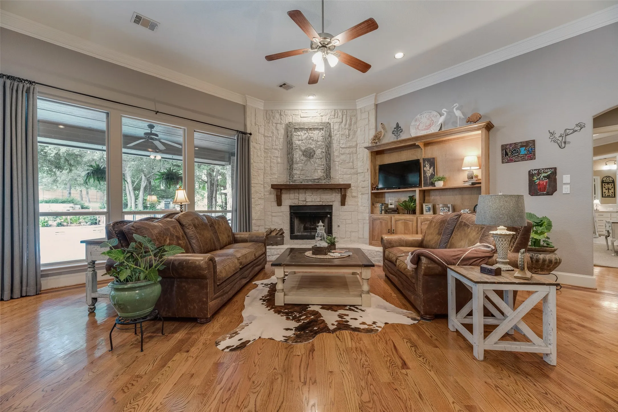 Living area with wood-finish flooring, a stone-clad fireplace with a wood mantel, and expansive windows providing outdoor views