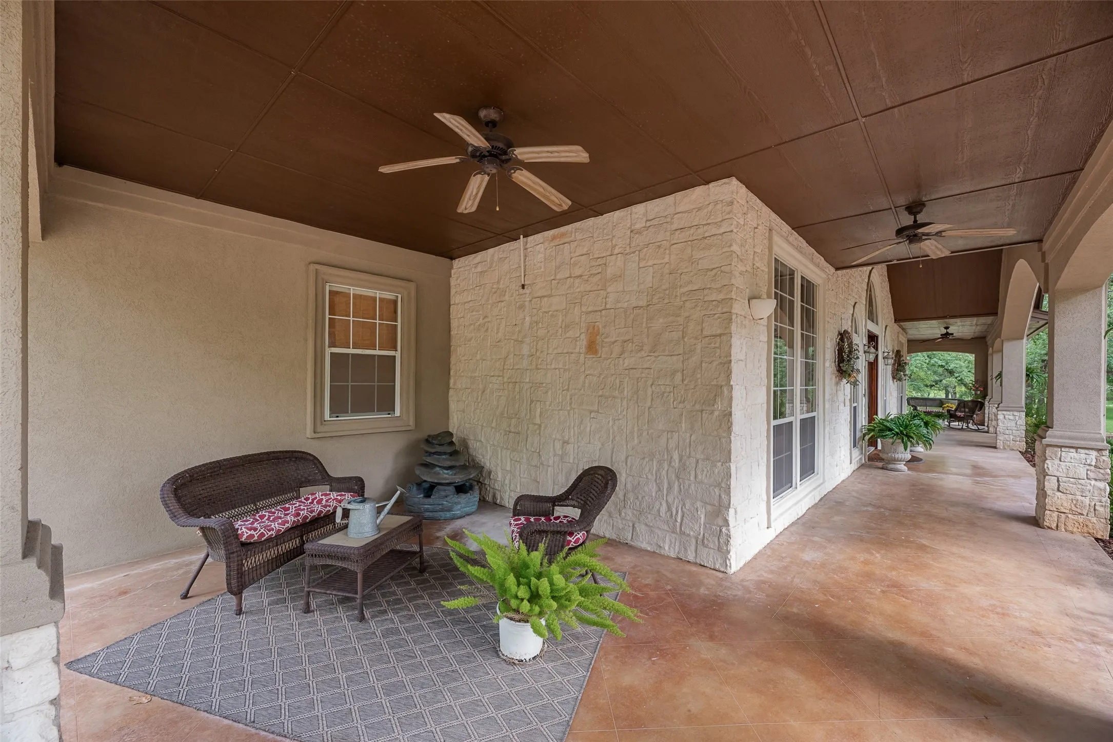 Expansive covered porch featuring a textured stucco finish, white stone accent wall, wood-paneled ceiling, and ceiling fans