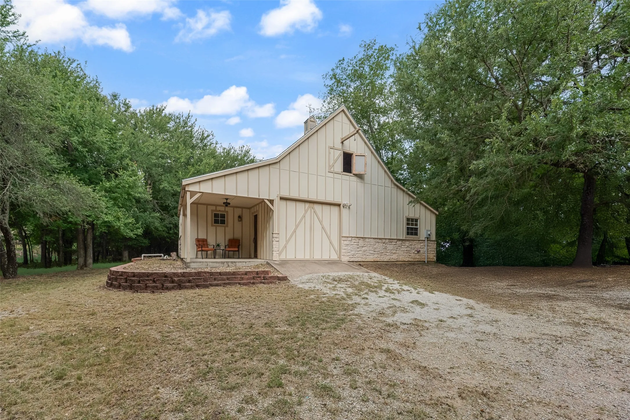 Barn-style structure featuring vertical siding, stone foundation, covered porch, and mature trees