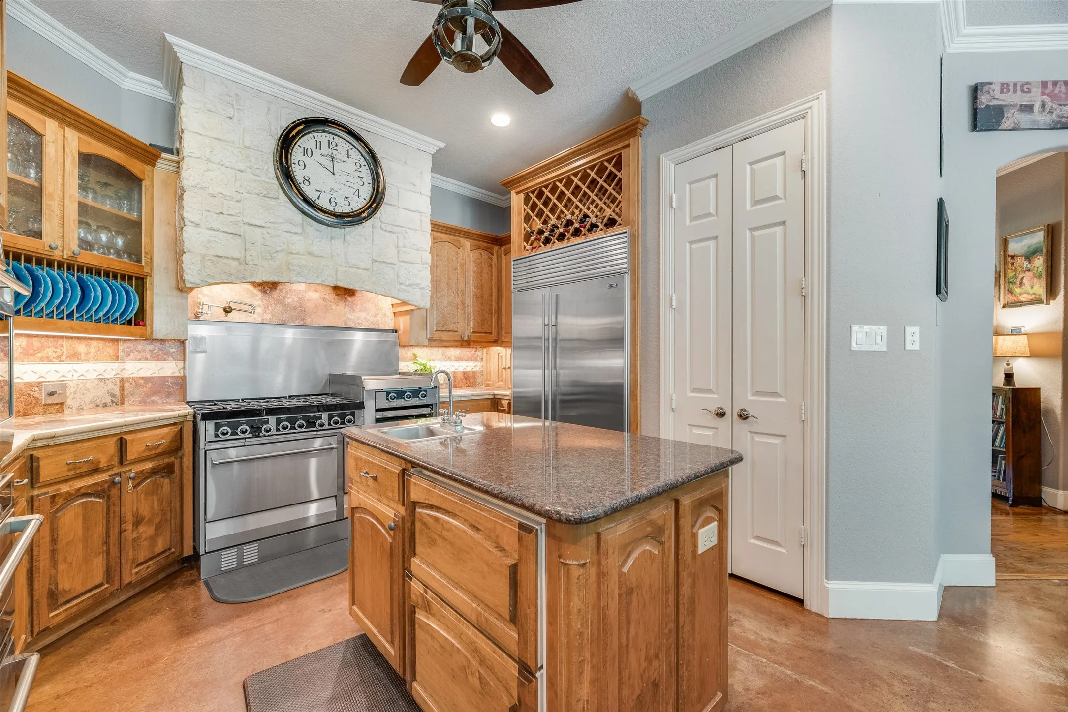 Gourmet kitchen featuring a stone-clad range hood, stainless steel professional-grade gas range, and a large center island with an integrated sink