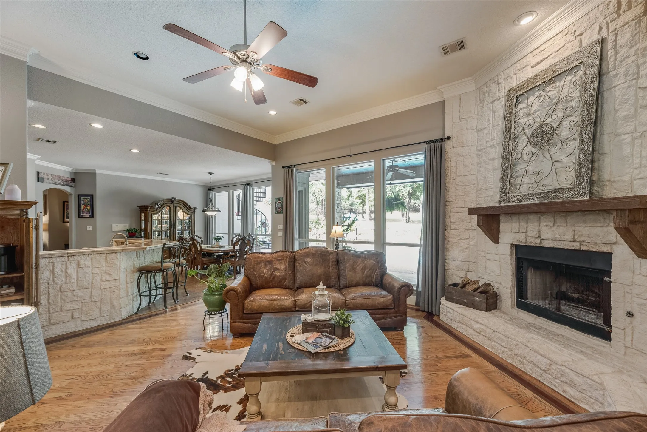 Living area featuring a stone fireplace with a wood mantel, wood-finish flooring, recessed lighting, and a ceiling fan