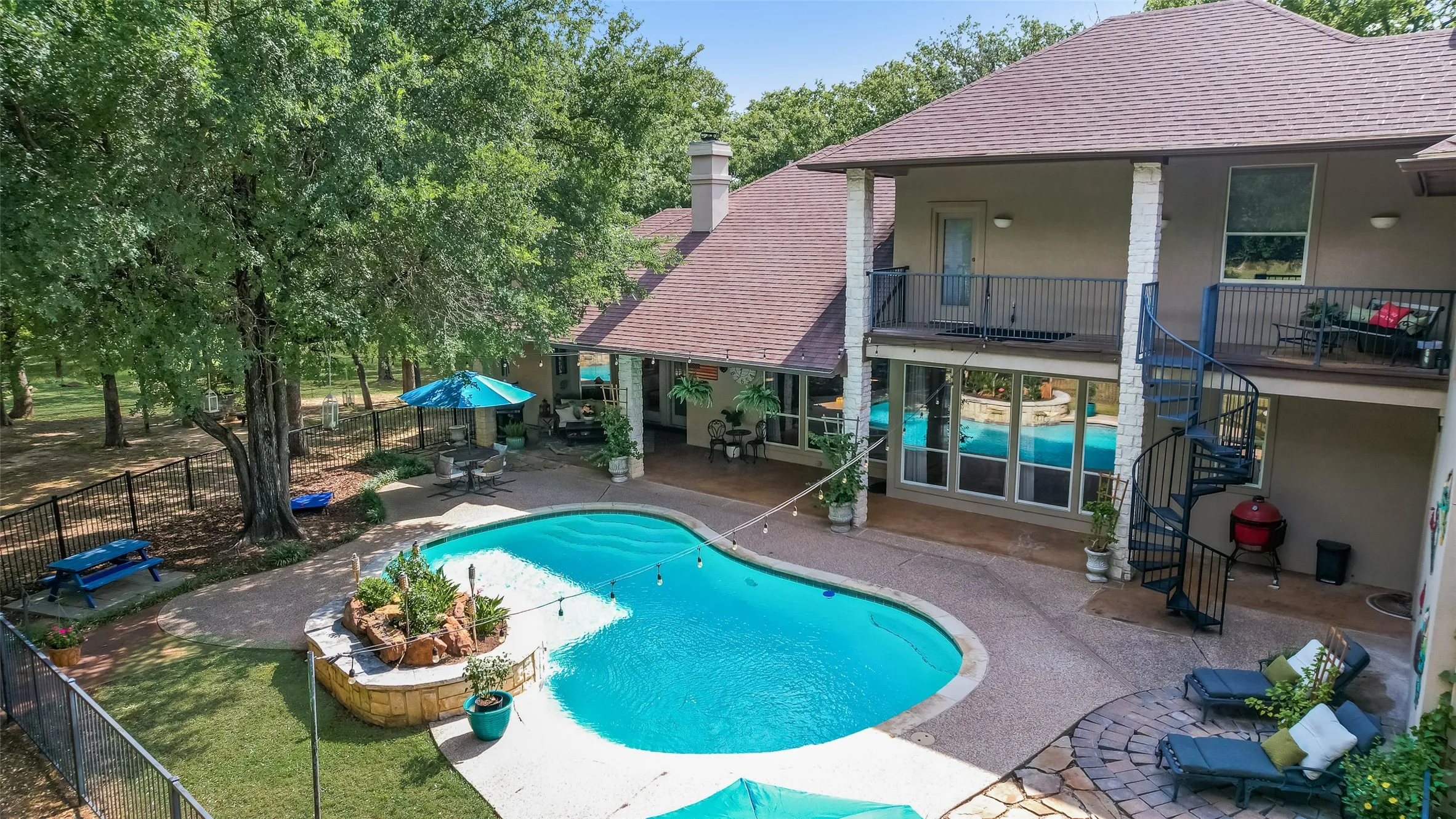Expansive outdoor living area featuring a freeform swimming pool, stone patio, and perimeter fencing