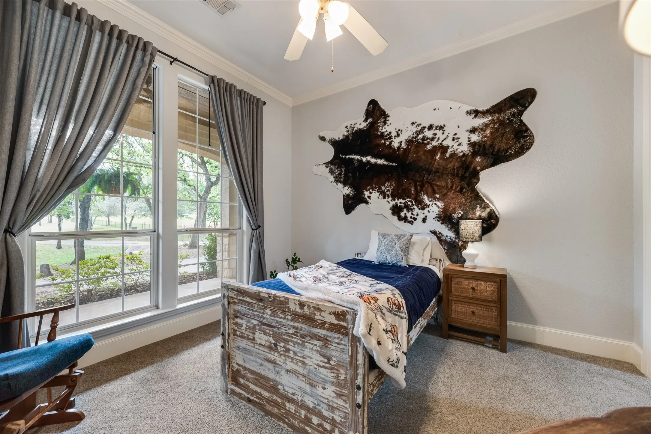 Carpeted room featuring large windows with exterior landscaping, crown molding, and a ceiling fan