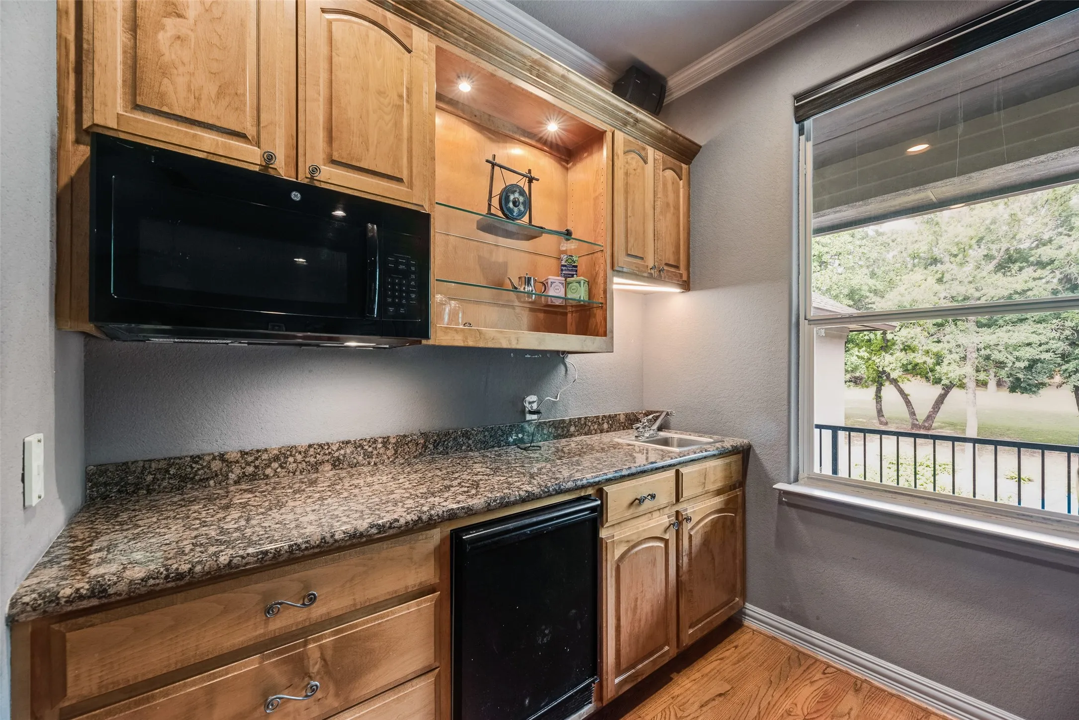 Wet bar featuring wooden cabinetry, speckled countertop, an undermount sink, built-in microwave, and a black beverage refrigerator