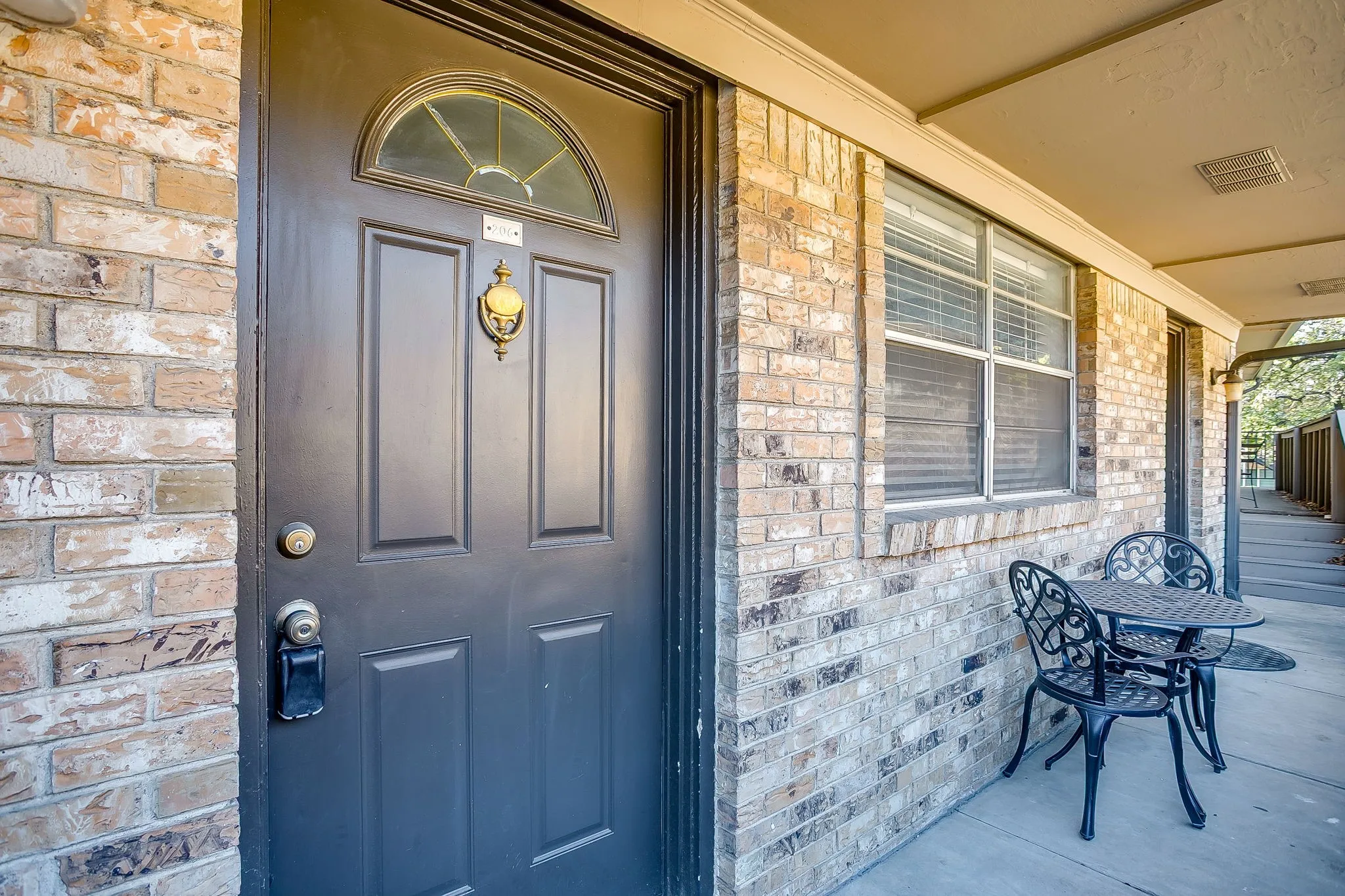 Brick exterior featuring a black paneled entry door with an arched transom window and a brass door knocker