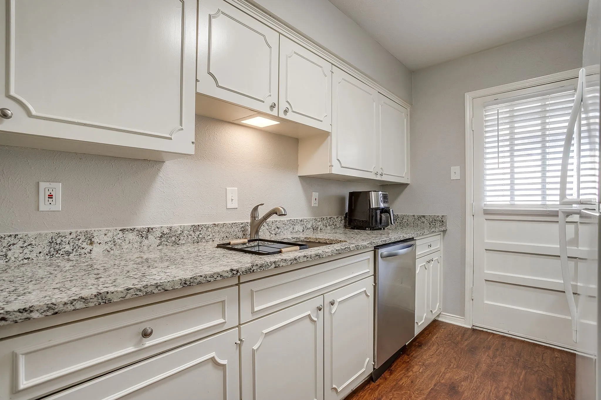 Kitchen featuring white cabinetry, speckled countertops, stainless steel sink with a high-arc faucet, stainless steel dishwasher, and wood-finish flooring