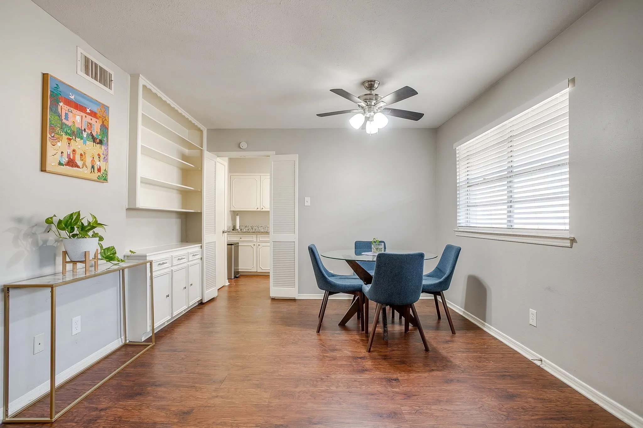 Open-concept room featuring wood-finish flooring, a ceiling fan with light fixture, and a window with blinds