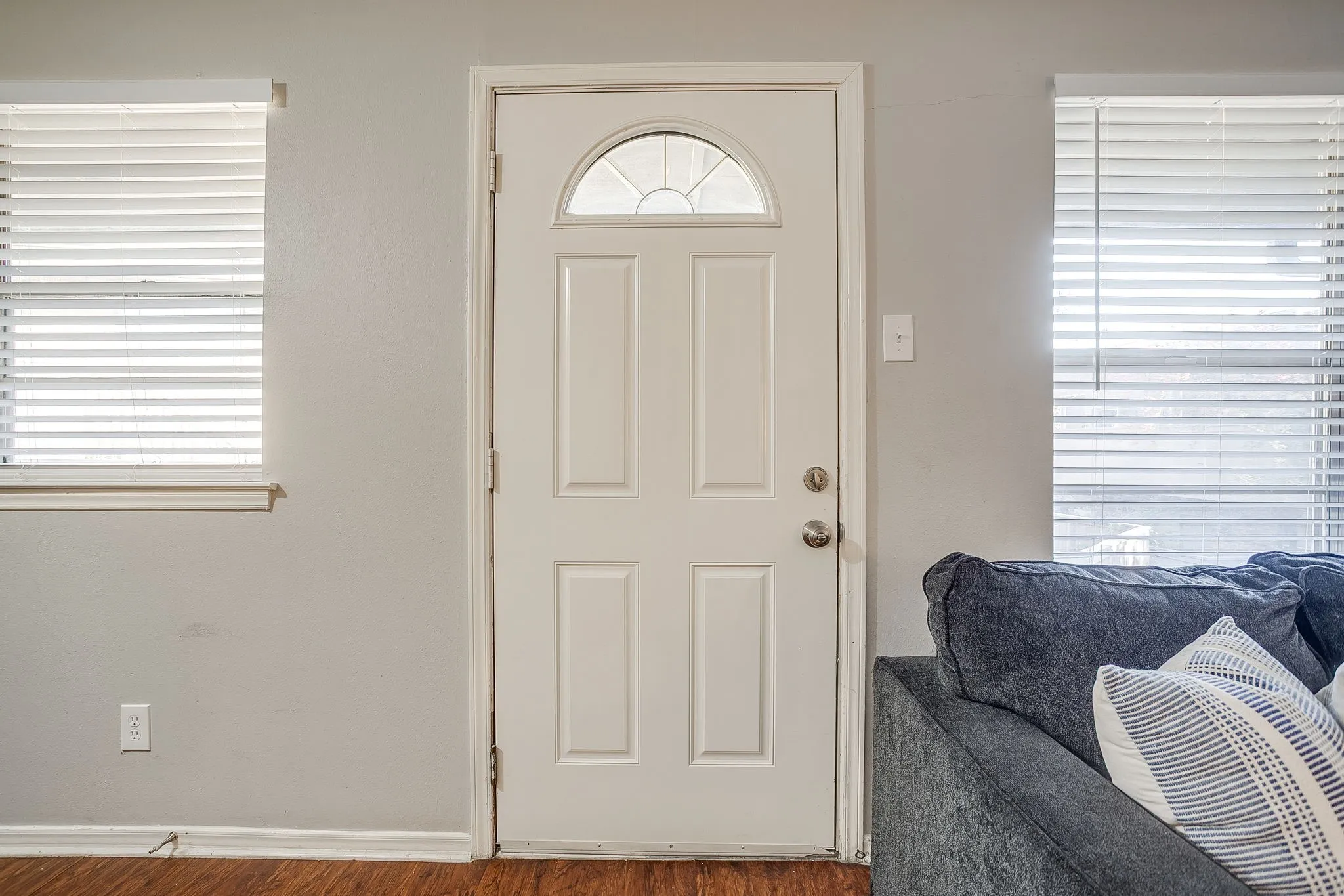 White paneled entry door with an arched glass insert, flanked by two windows fitted with horizontal blinds