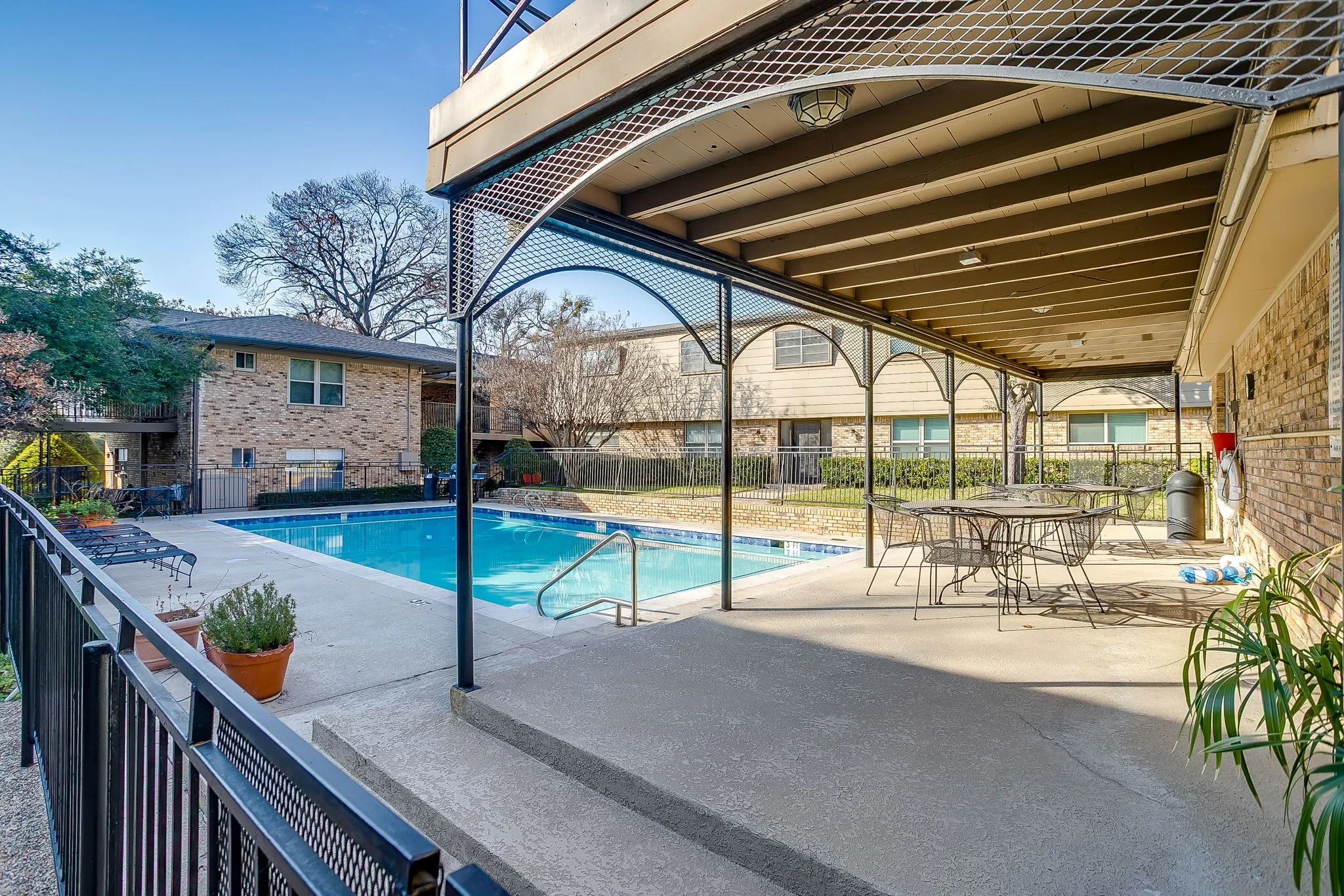 Inviting outdoor pool area featuring a rectangular swimming pool, concrete decking, and a covered patio with overhead lighting