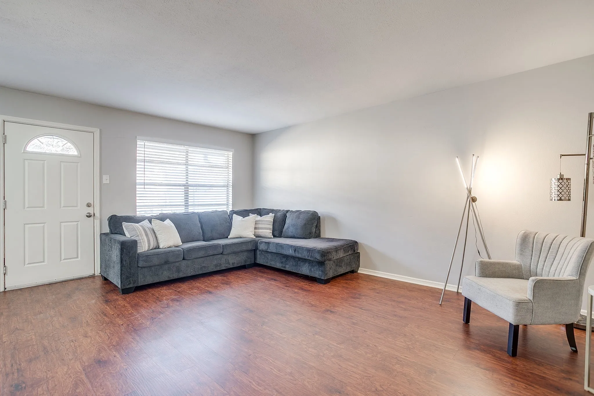 Spacious living area featuring wood-finish flooring, light-colored walls, and a multi-paned window with blinds