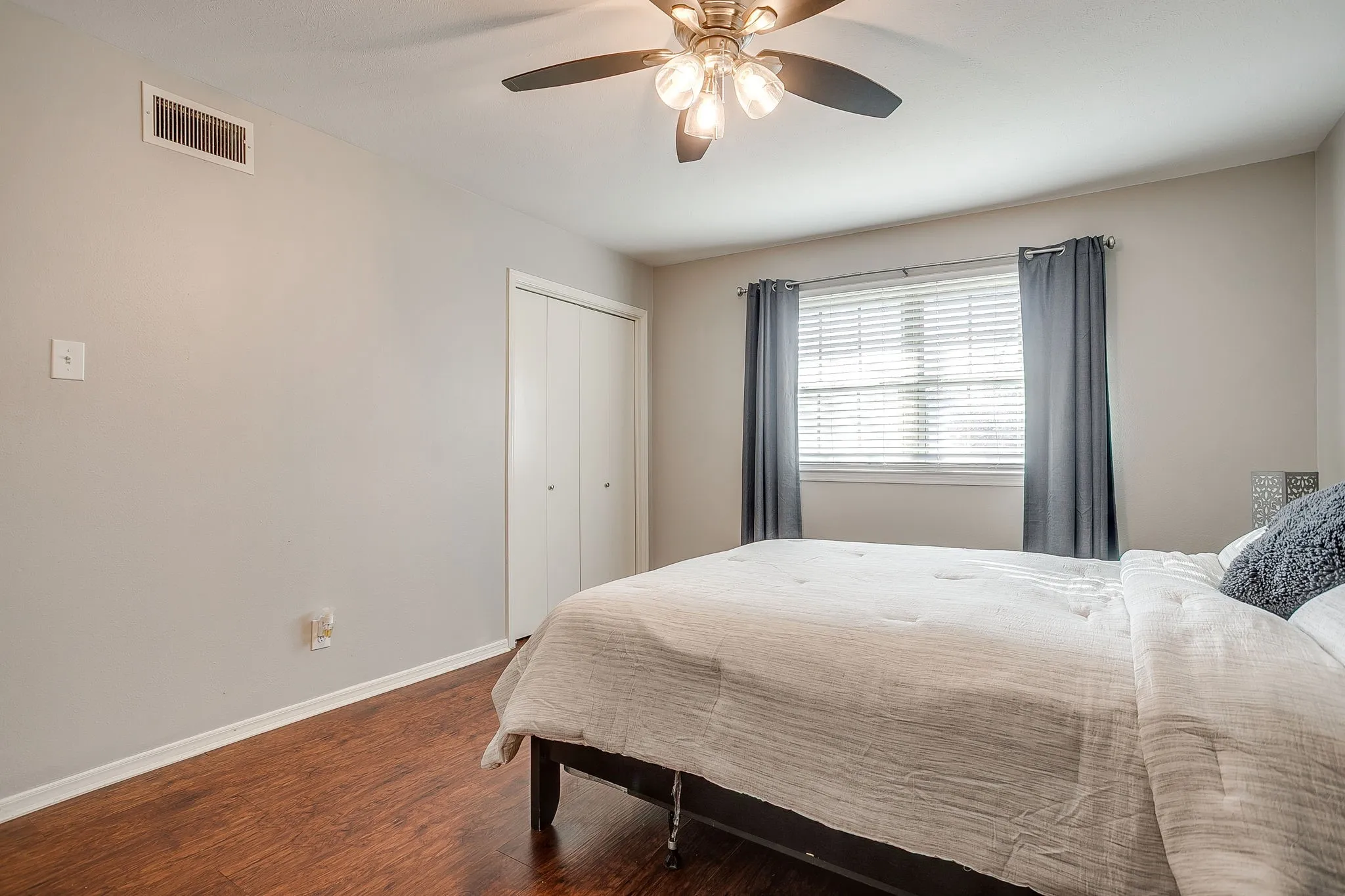 Spacious room featuring wood-finish flooring, a ceiling fan with integrated lighting, and a window with horizontal blinds