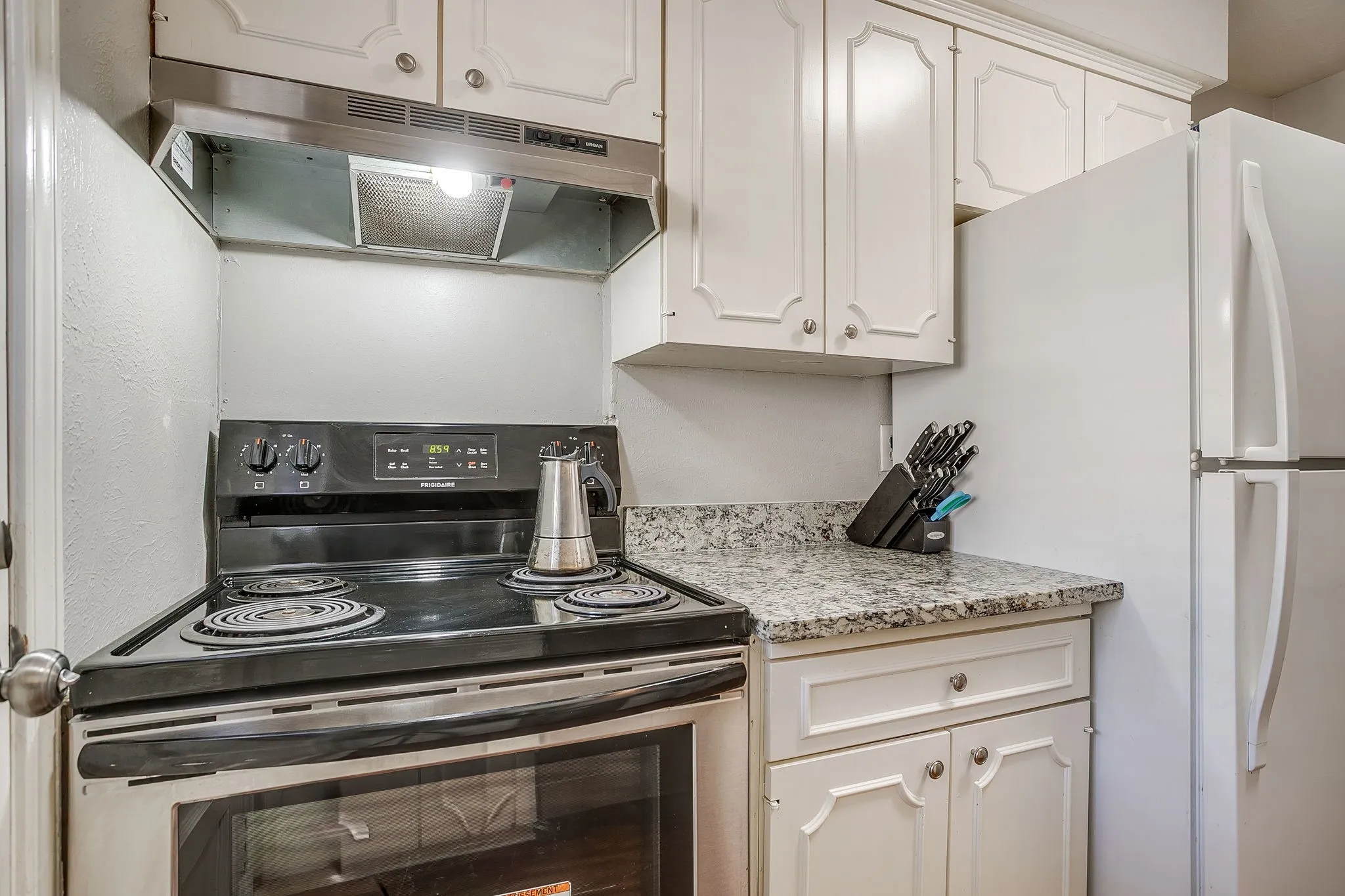 Kitchen featuring a freestanding black electric range, stainless steel range hood, white cabinetry, and a light-toned countertop