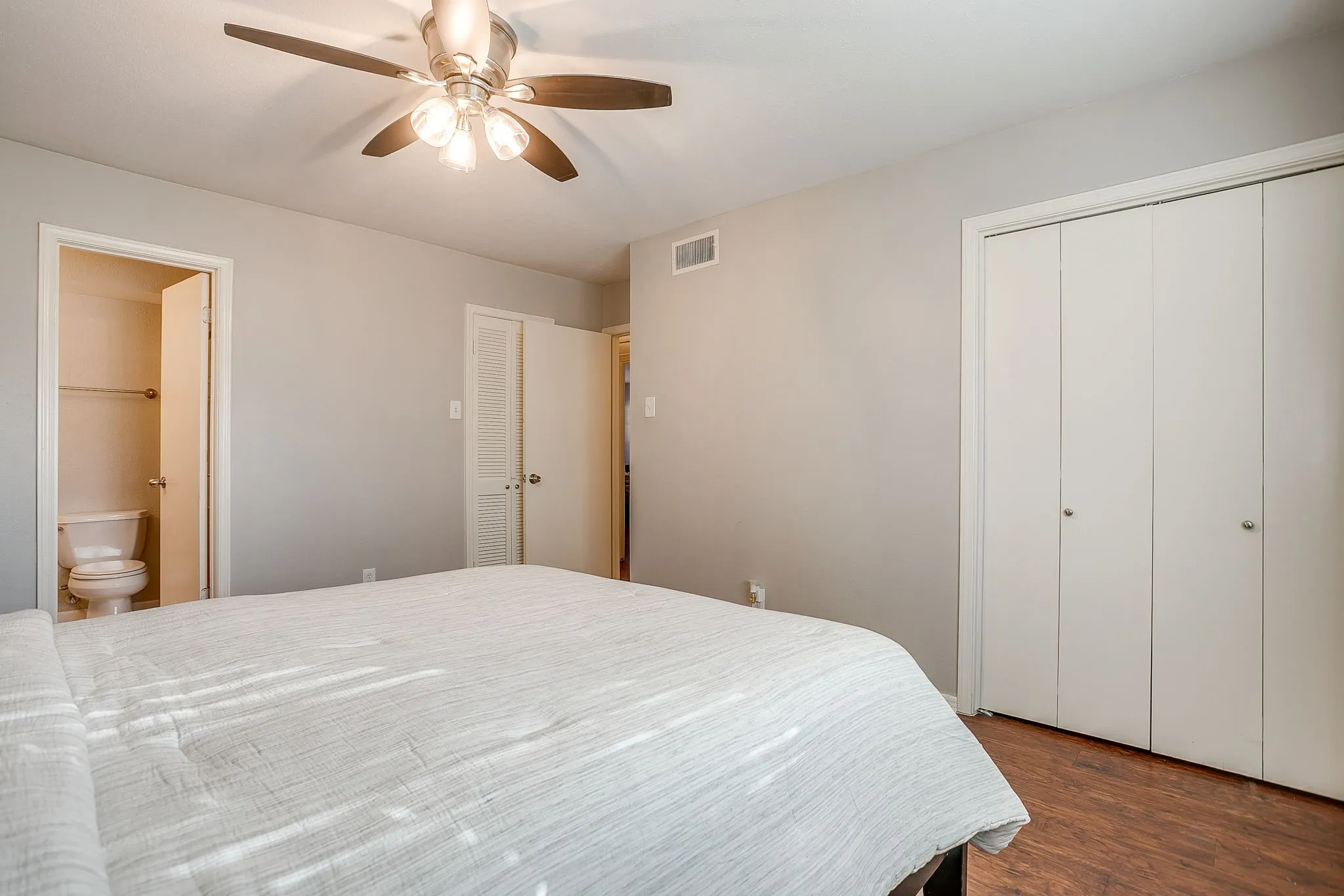 Bedroom featuring a ceiling fan with integrated lighting, wood-finish flooring, and bi-fold closet doors