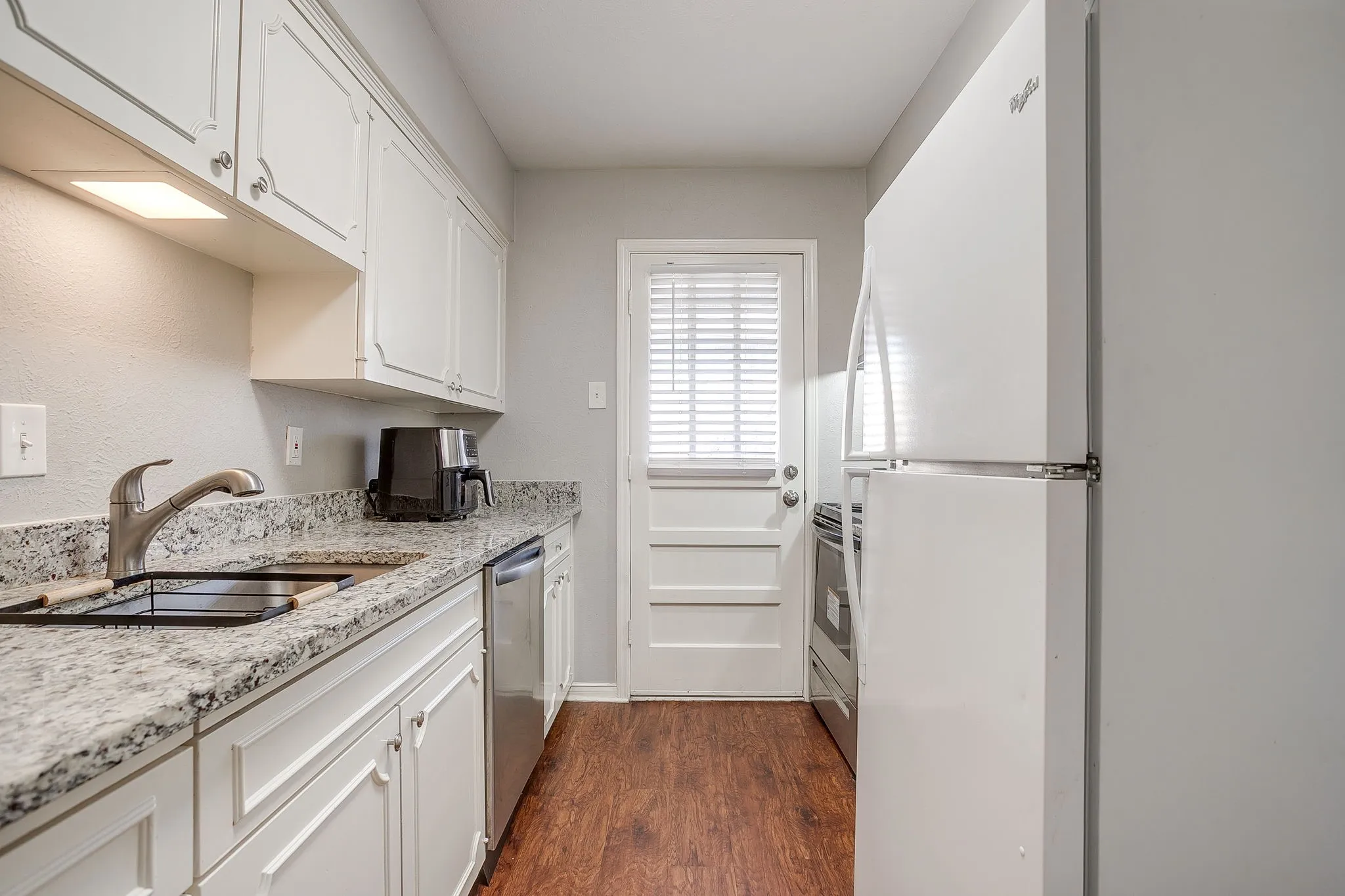 Kitchen featuring white cabinetry with silver hardware, granite-style countertops, stainless steel sink with a gooseneck faucet, and wood-finish flooring