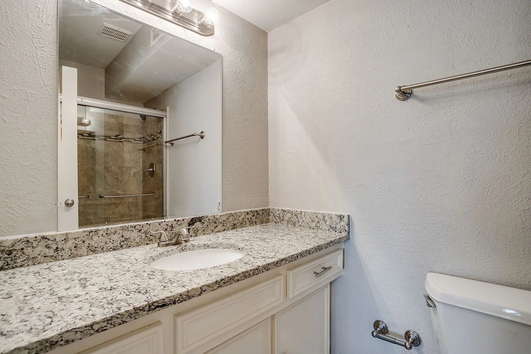 Bathroom vanity with a speckled countertop, undermount sink, and a chrome faucet