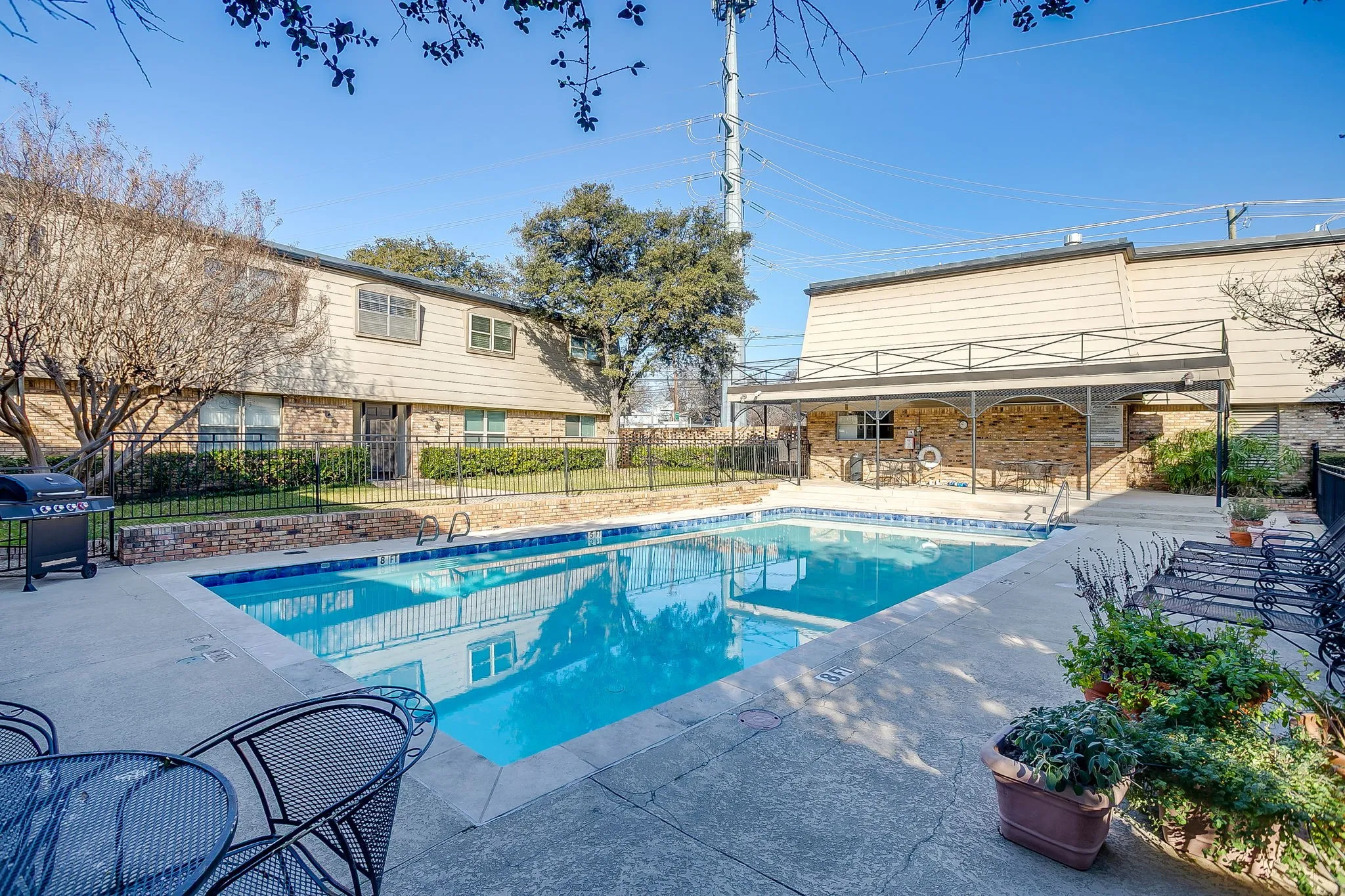 Outdoor swimming pool with concrete decking, surrounded by a metal fence and mature landscaping