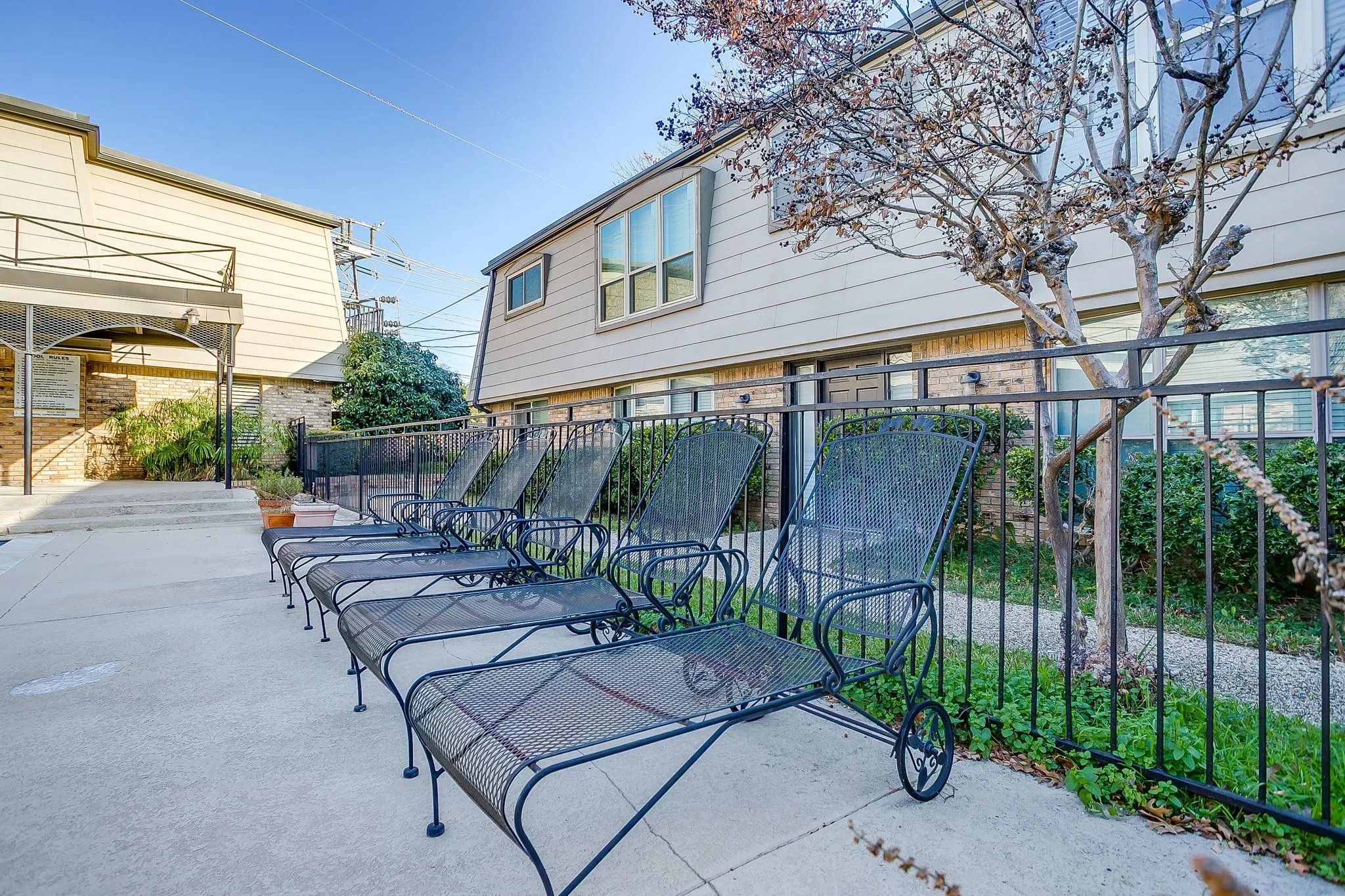 Concrete patio area bordered by a black wrought iron fence and mature trees