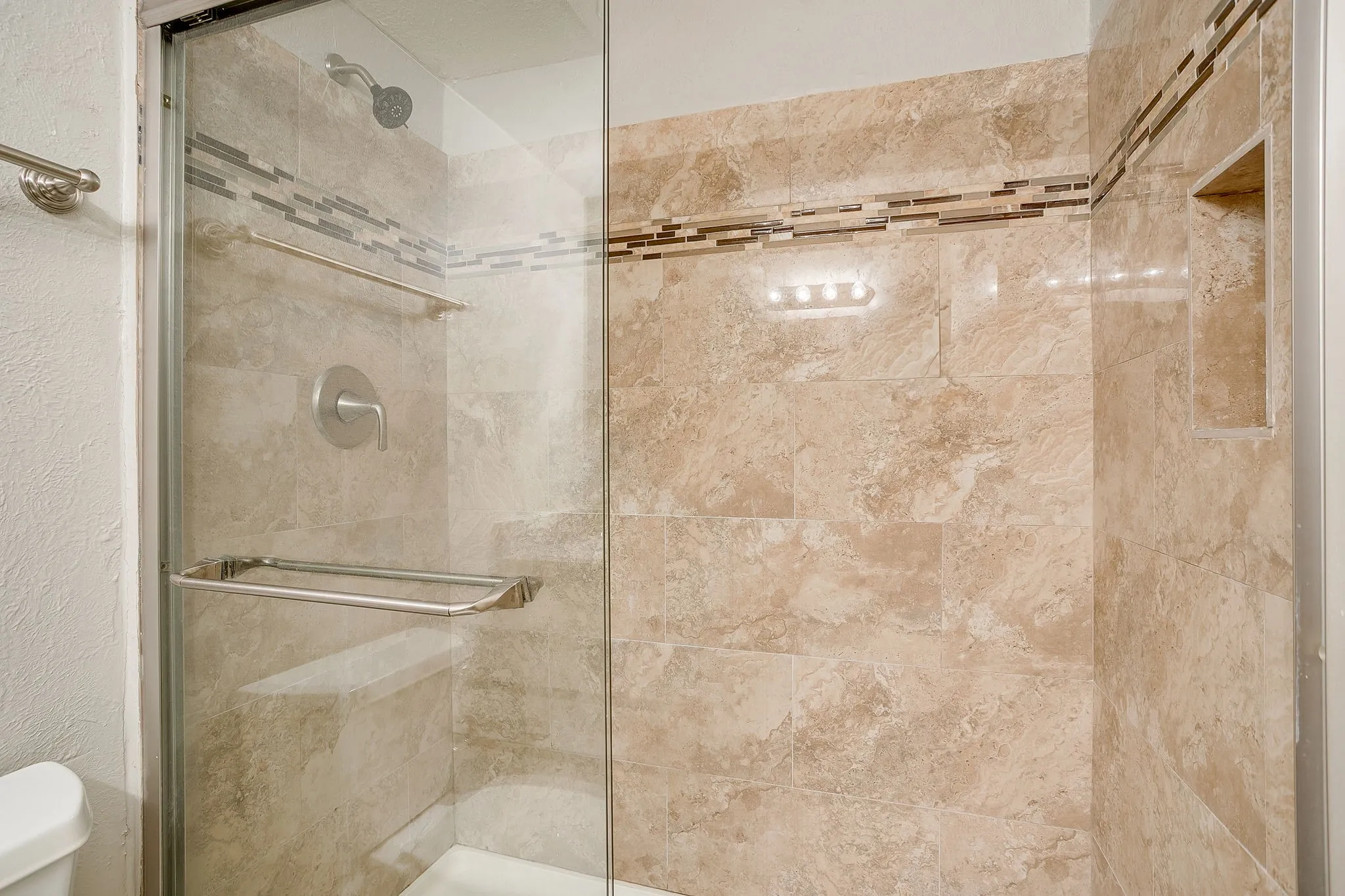 Tiled shower enclosure featuring a glass door, mosaic accent band, recessed niche, and a chrome shower head with coordinating hardware