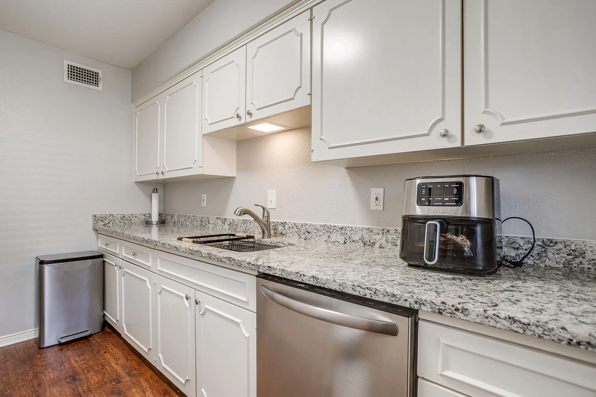 Kitchen featuring white shaker-style cabinetry, a stainless steel sink with a single-handle faucet, a built-in stainless steel dishwasher, speckled countertops, and wood-finish flooring