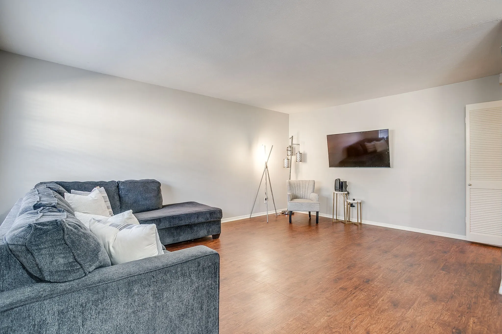 Spacious living area featuring wood-finish flooring, light gray walls, and a wall-mounted television