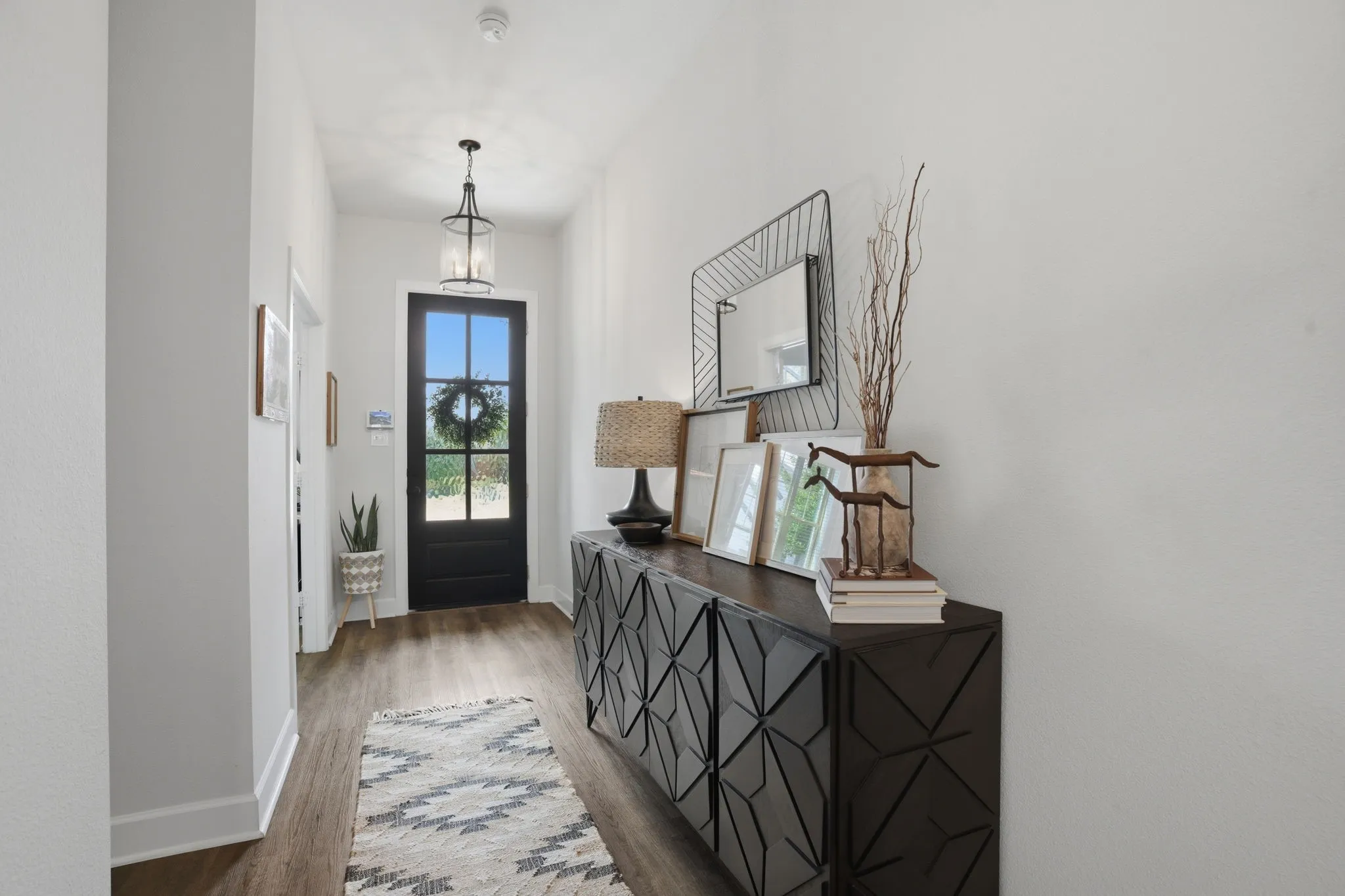 The entryway featuring a black, multi-pane door, complemented by wood-look flooring and a stylish glass lantern-style ceiling fixture that adds a touch of elegance and warmth to the space.
