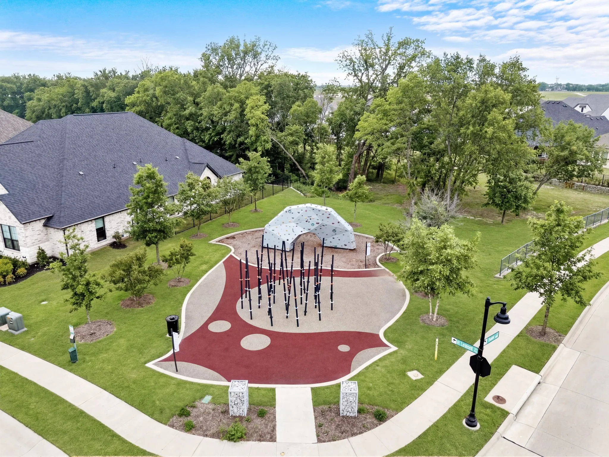 This vibrant community playground offers a fun and safe environment for children, featuring a variety of climbing equipment to encourage physical activity and imagination, complemented by soft ground surfacing to ensure a secure play experience. The area is beautifully shaded by mature trees, creating a natural and inviting atmosphere for playtime and exploration.