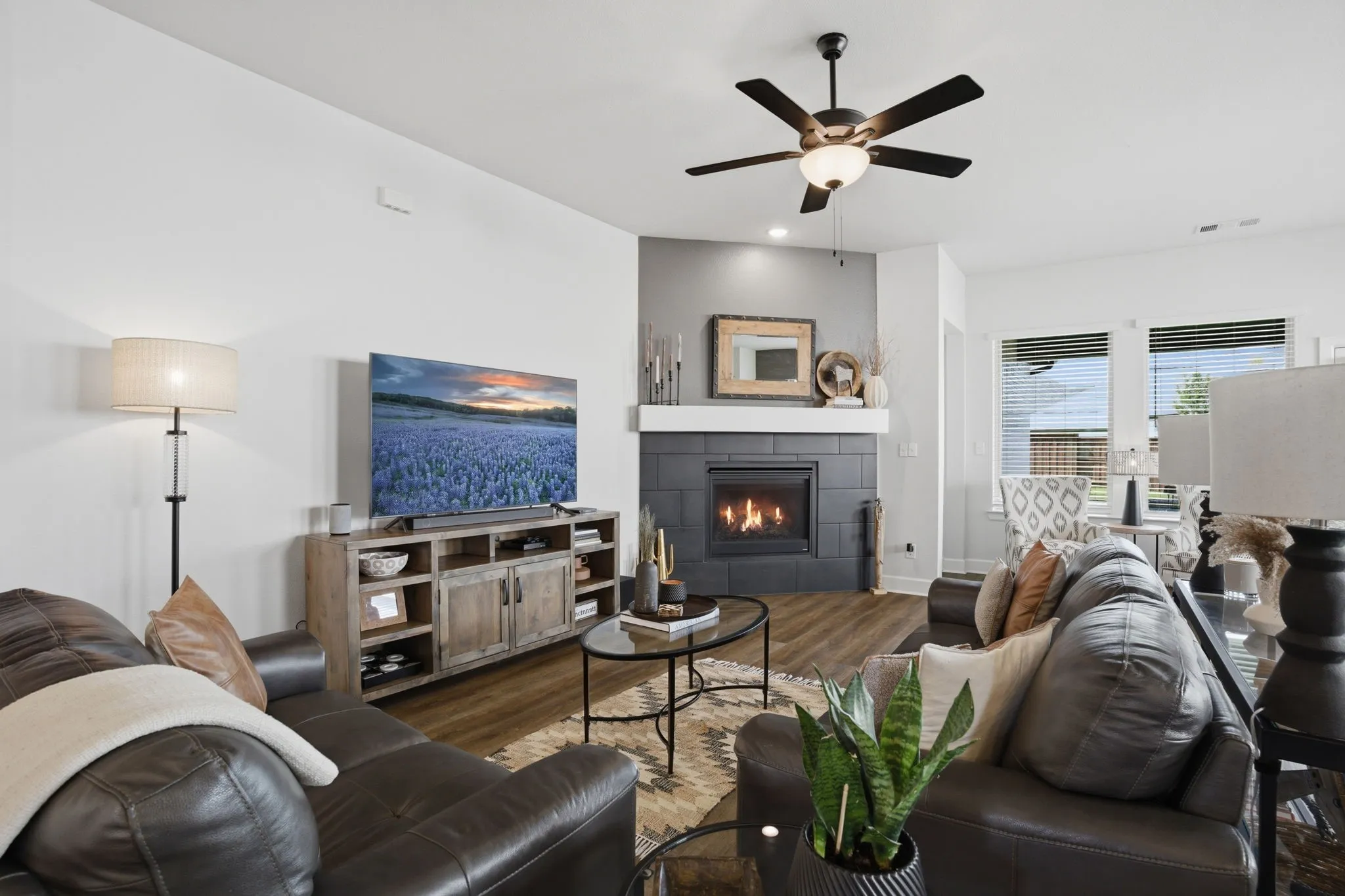 This open and inviting living area boasts ample space, complemented by durable wood-look flooring and a practical ceiling fan for optimal comfort. The focal point is undoubtedly the cozy fireplace, enhanced by a stylishly painted accent wall that adds personality and warmth to the entire space.