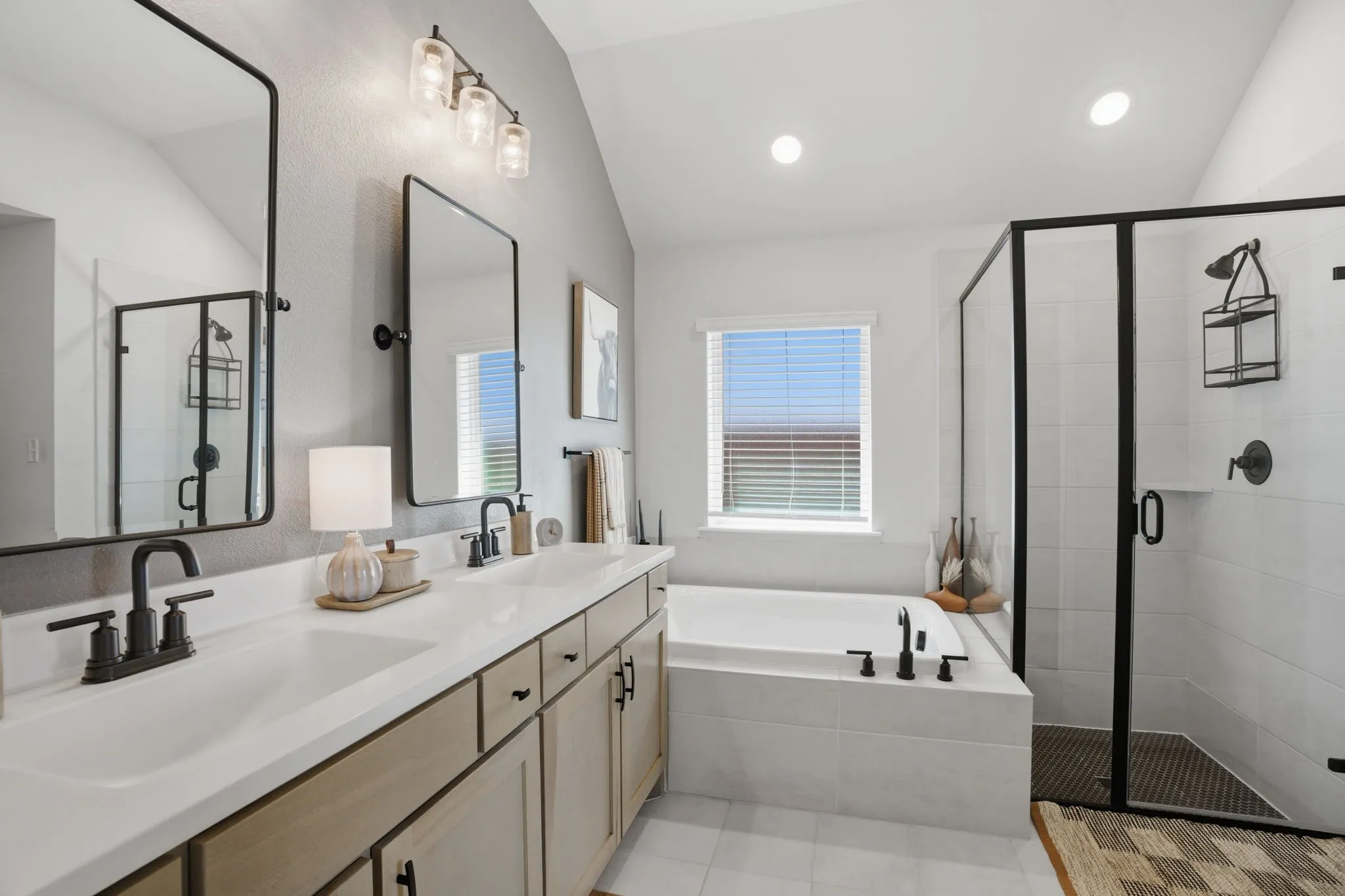 This image showcases a different perspective of the primary bathroom, highlighting the incorporated soaking tub and the modern glass-enclosed shower, which is beautifully accented by its sleek, black frame detail.