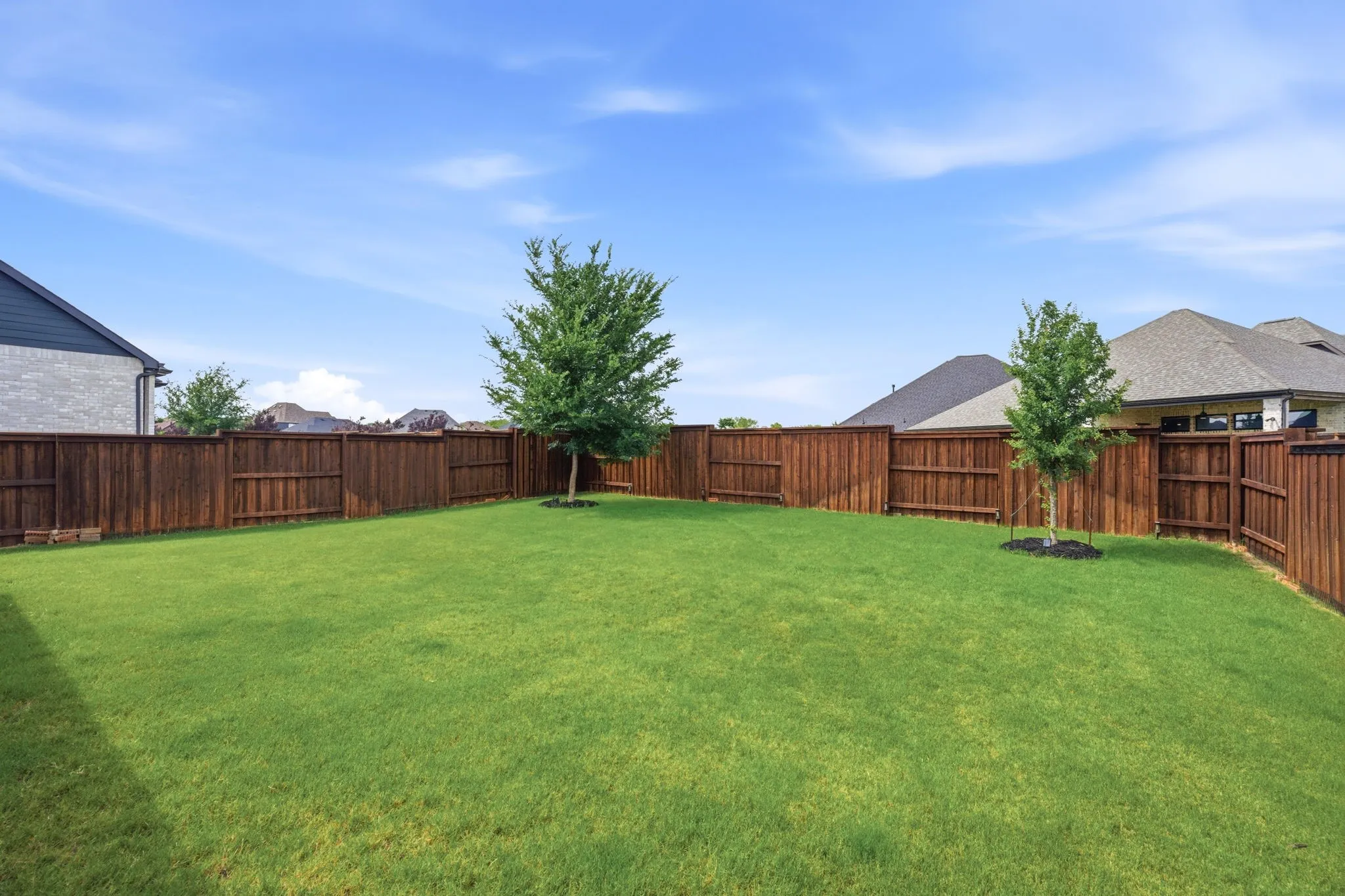 This photo showcases a large, inviting backyard featuring a well-maintained, green lawn, complemented by strategically placed privacy fencing to ensure seclusion, and the promise of future beauty with two young, growing trees adding character and potential shade to the space.