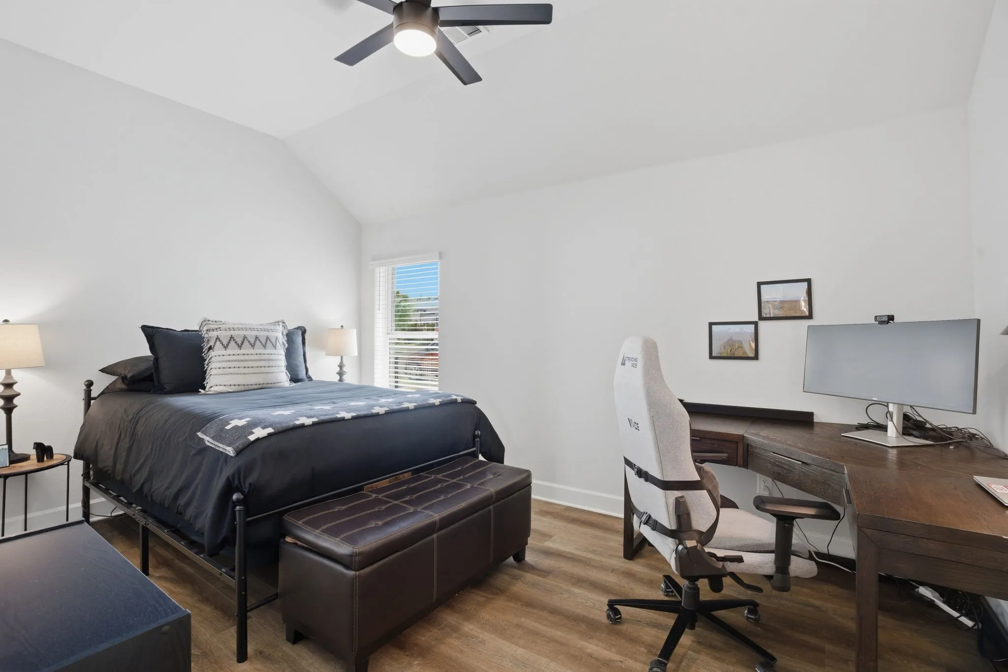 This spacious secondary bedroom features a high ceiling that enhances the sense of openness, complemented by attractive wood-look flooring for warmth and style. A convenient ceiling fan ensures comfortable air circulation, and the room offers ample wall space, providing excellent options for furniture placement and personal touches, making it a versatile and inviting space.