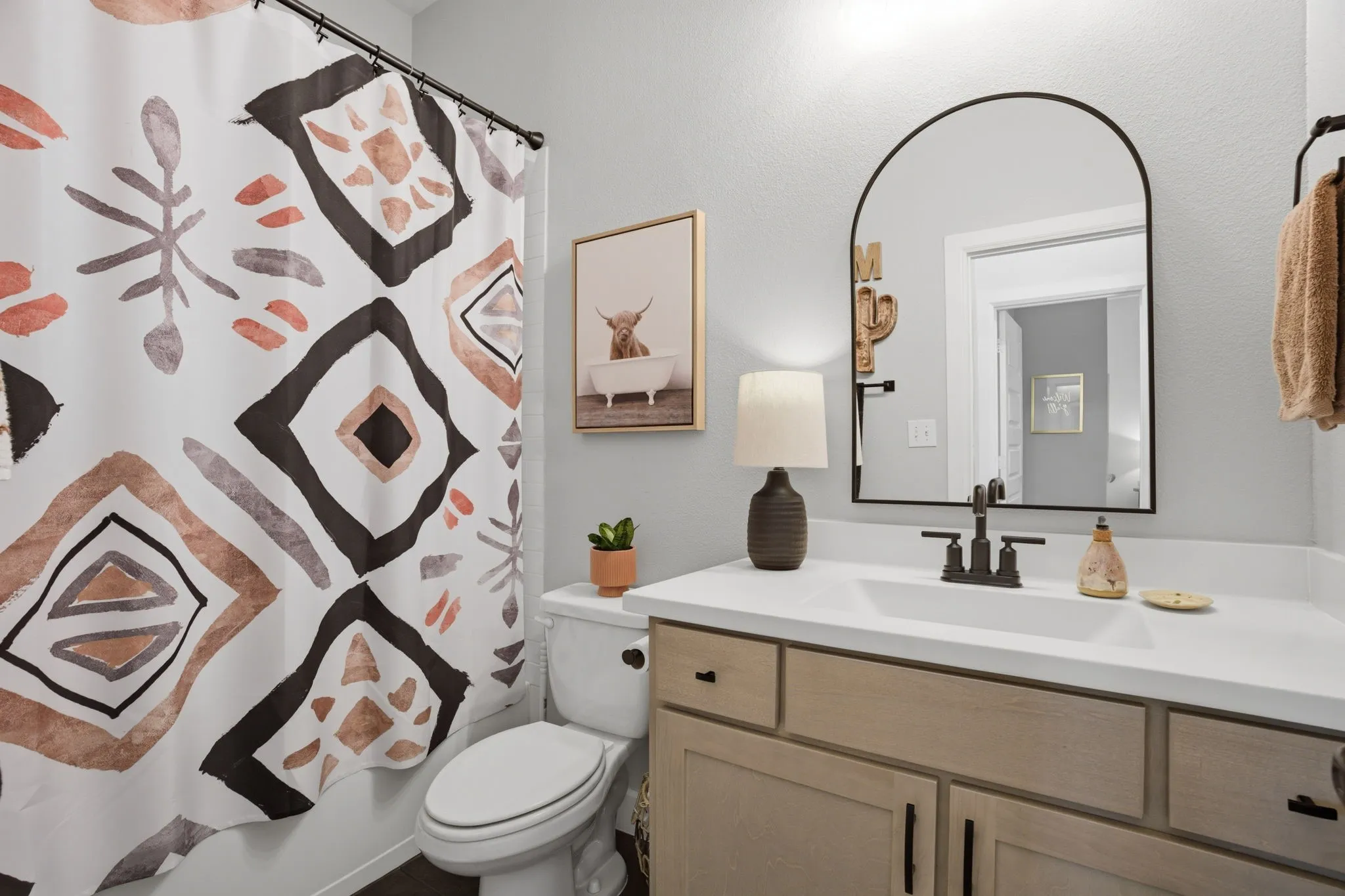 Detailed view of the secondary bathroom showcasing a light-toned vanity complemented by sleek black hardware, a pristine white countertop, and a functional undermount sink. The bathroom features a convenient shower/tub combination, offering versatile bathing options.