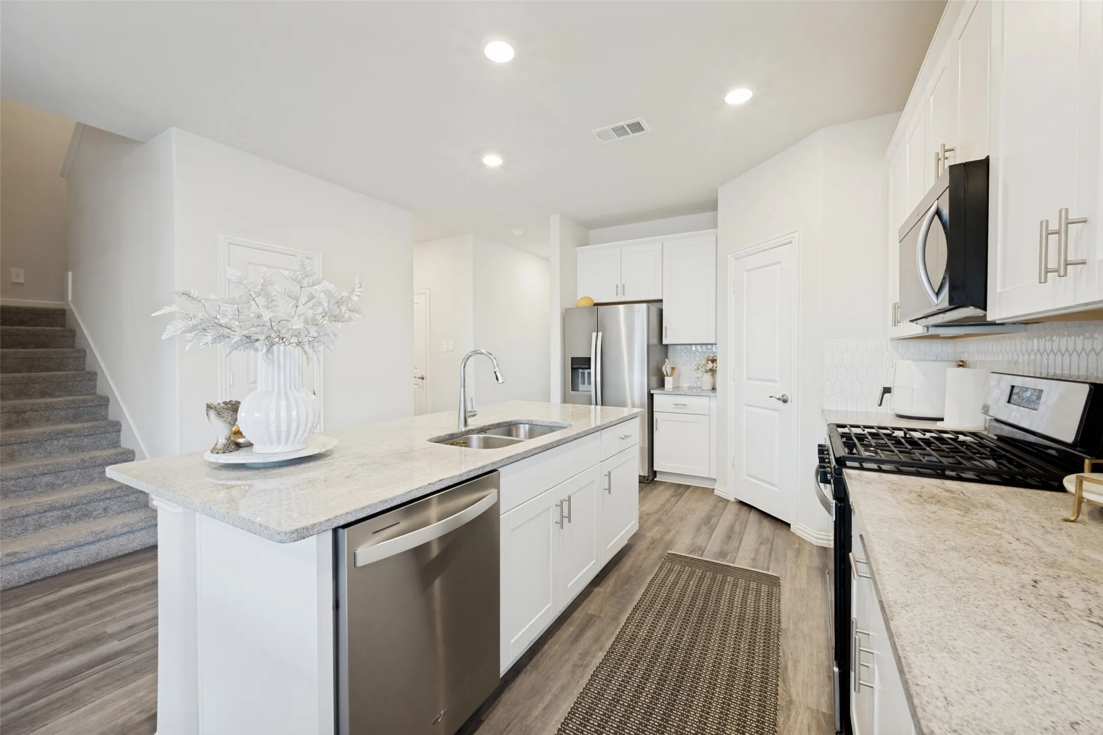 Modern kitchen featuring an island with a double basin sink, stainless steel dishwasher, and light-toned countertop