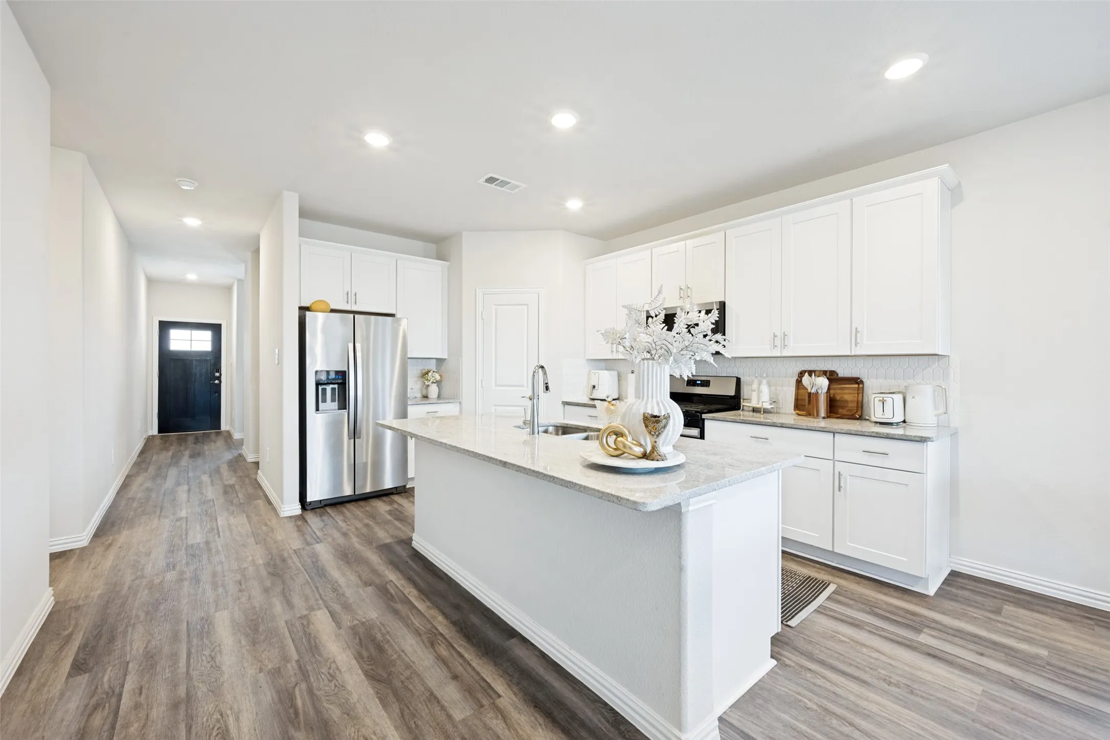 Modern kitchen featuring white cabinetry, light-toned countertops, stainless steel appliances, and a central island with an integrated sink