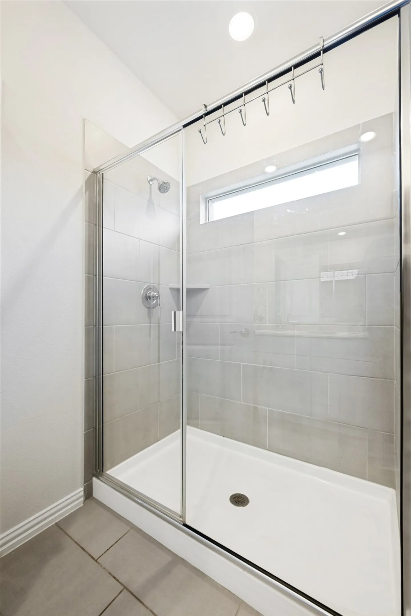 Glass-enclosed shower featuring a tiled surround, recessed shelf, and an overhead transom window